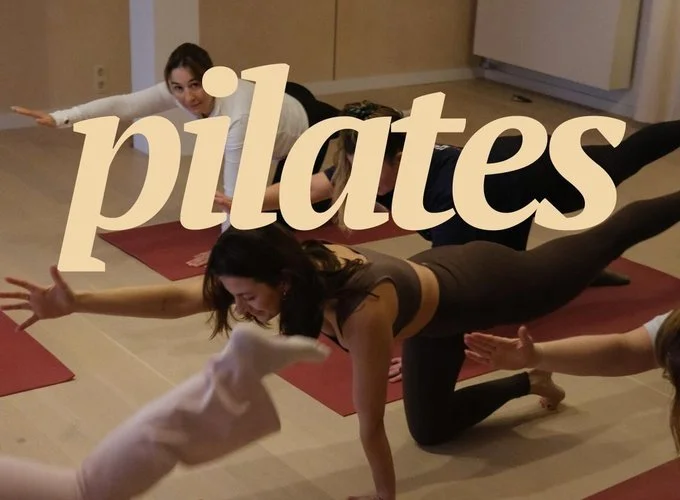 Mensen die pilates oefeningen doen in een sportschool, met een vrouw in een plankpositie en anderen die mee doen.