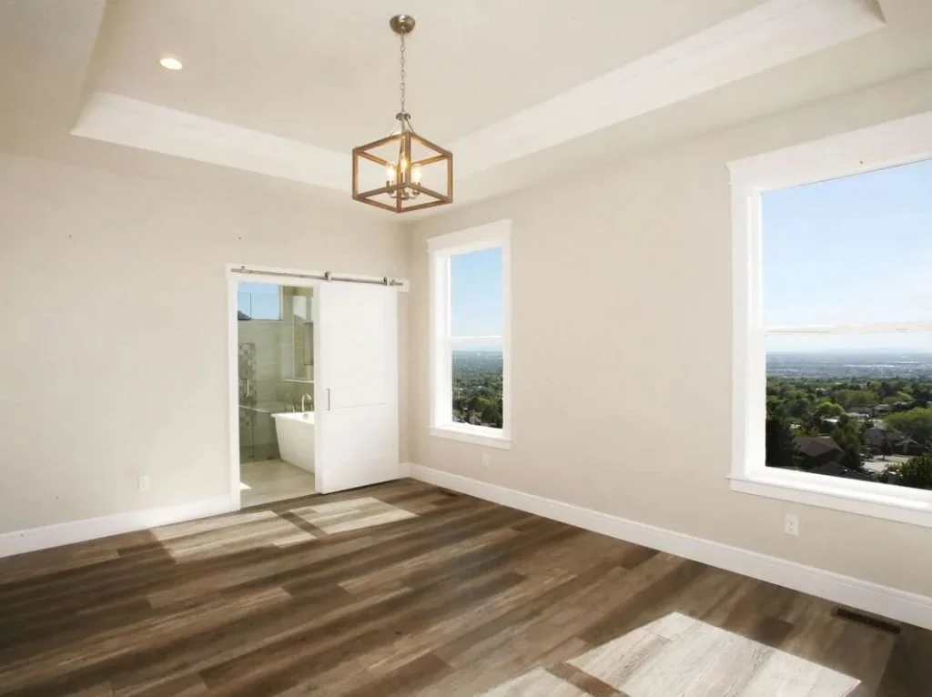 Empty room with large windows, wooden floor, and an en suite bathroom with glass door.