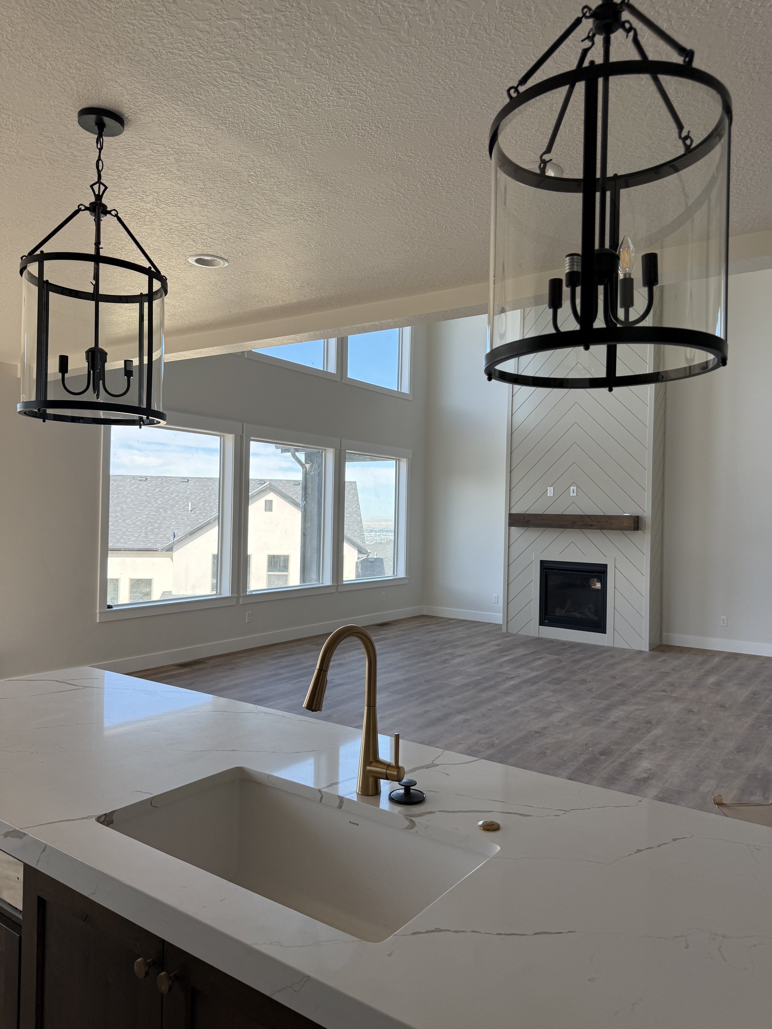 Open-concept living space with large windows, a modern fireplace, and two circular black chandeliers hanging from the ceiling.