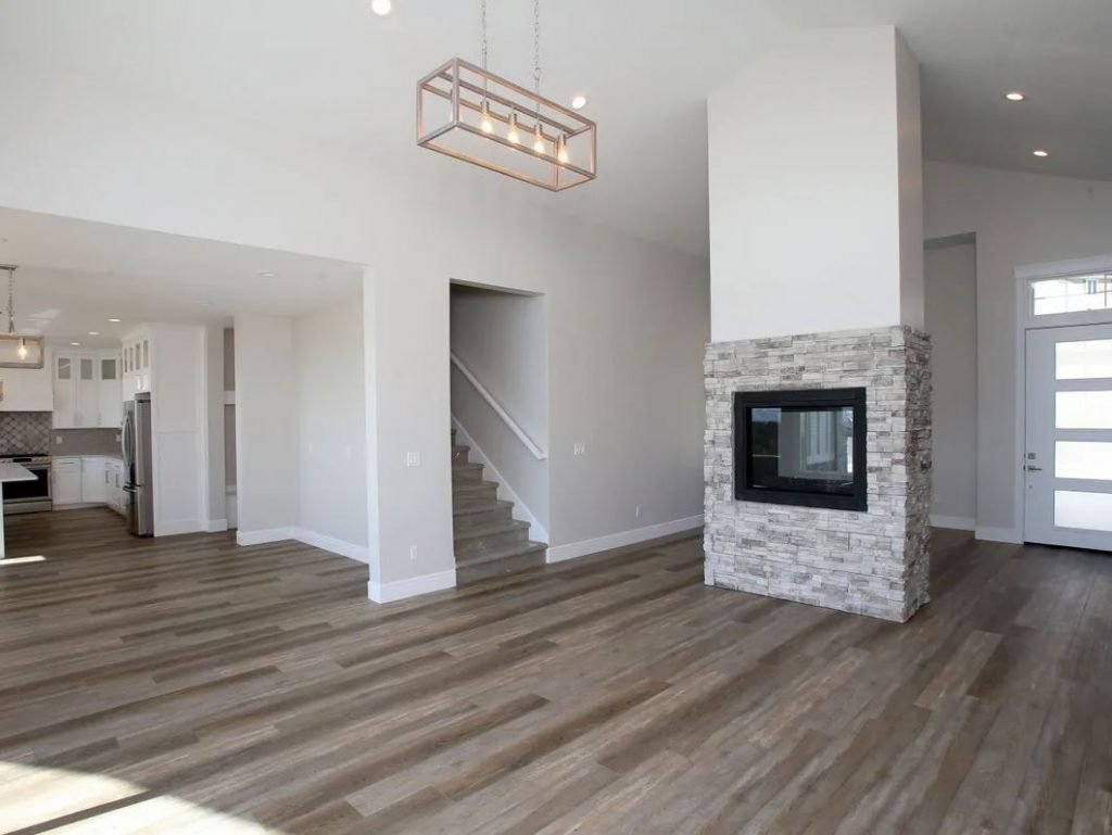 Living room with hardwood floors, a modern fireplace with stone surround, white walls, a staircase, and a doorway leading outside.