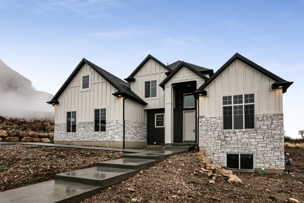 Newly constructed house with white siding and stone accents, set in a rural landscape with mountains in the background.