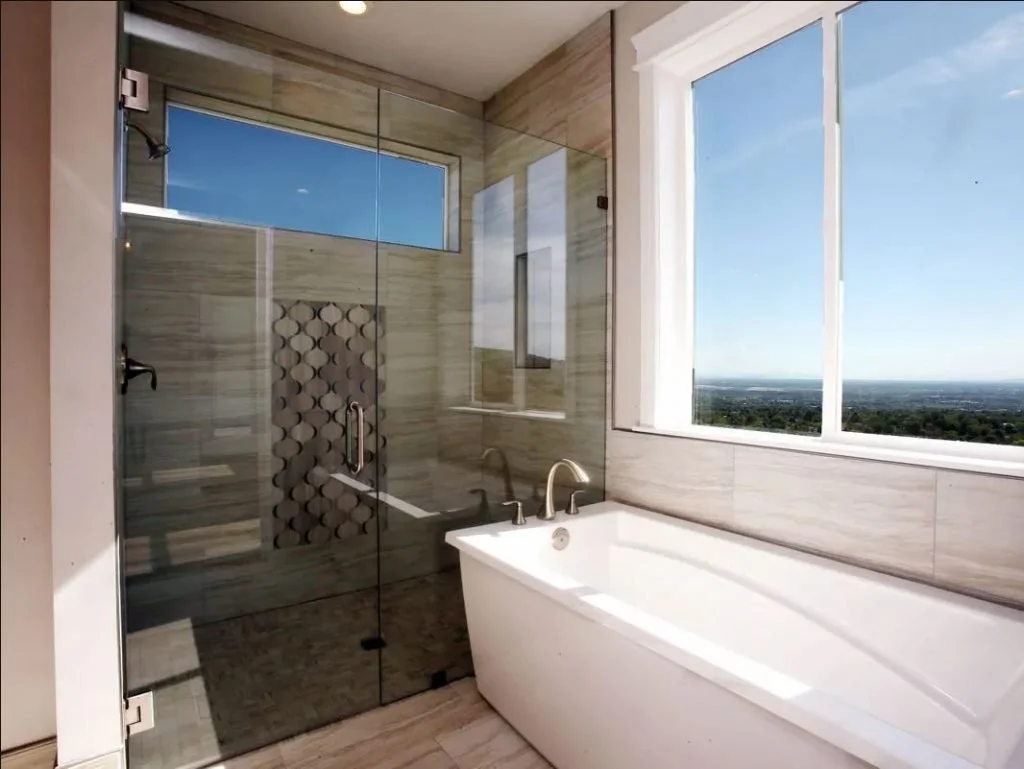 Modern bathroom with a large white bathtub and a glass-enclosed shower area, featuring a window with a scenic view.