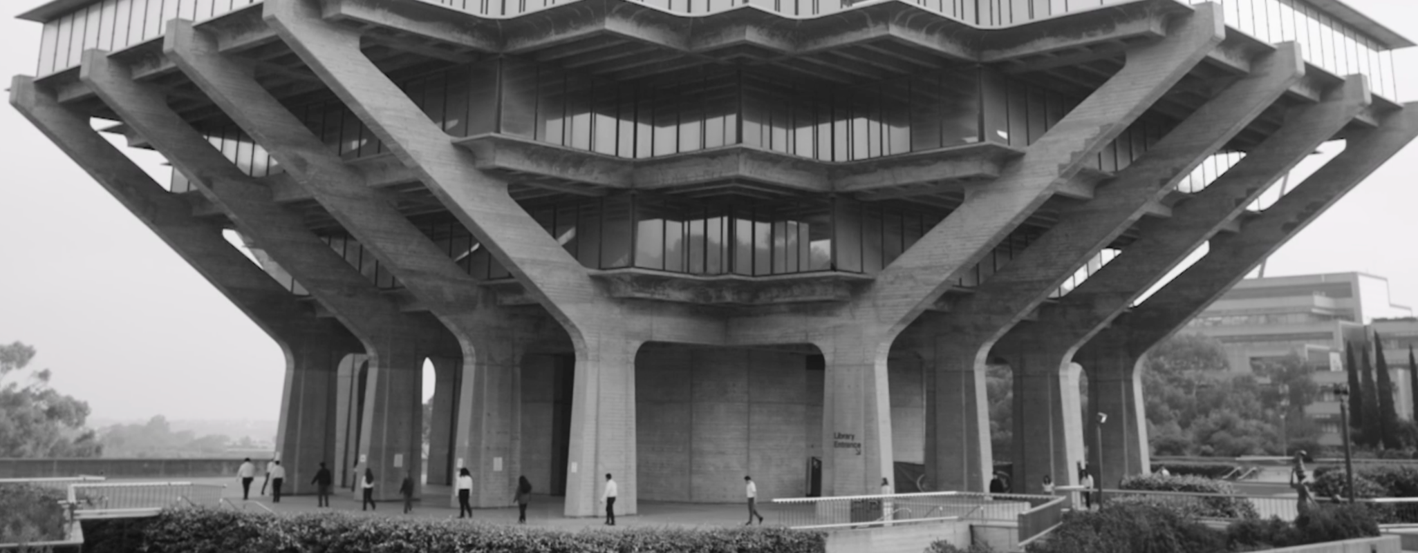 A modern architectural building with a geometric concrete structure and multiple levels, seen from below, with people walking at the base.