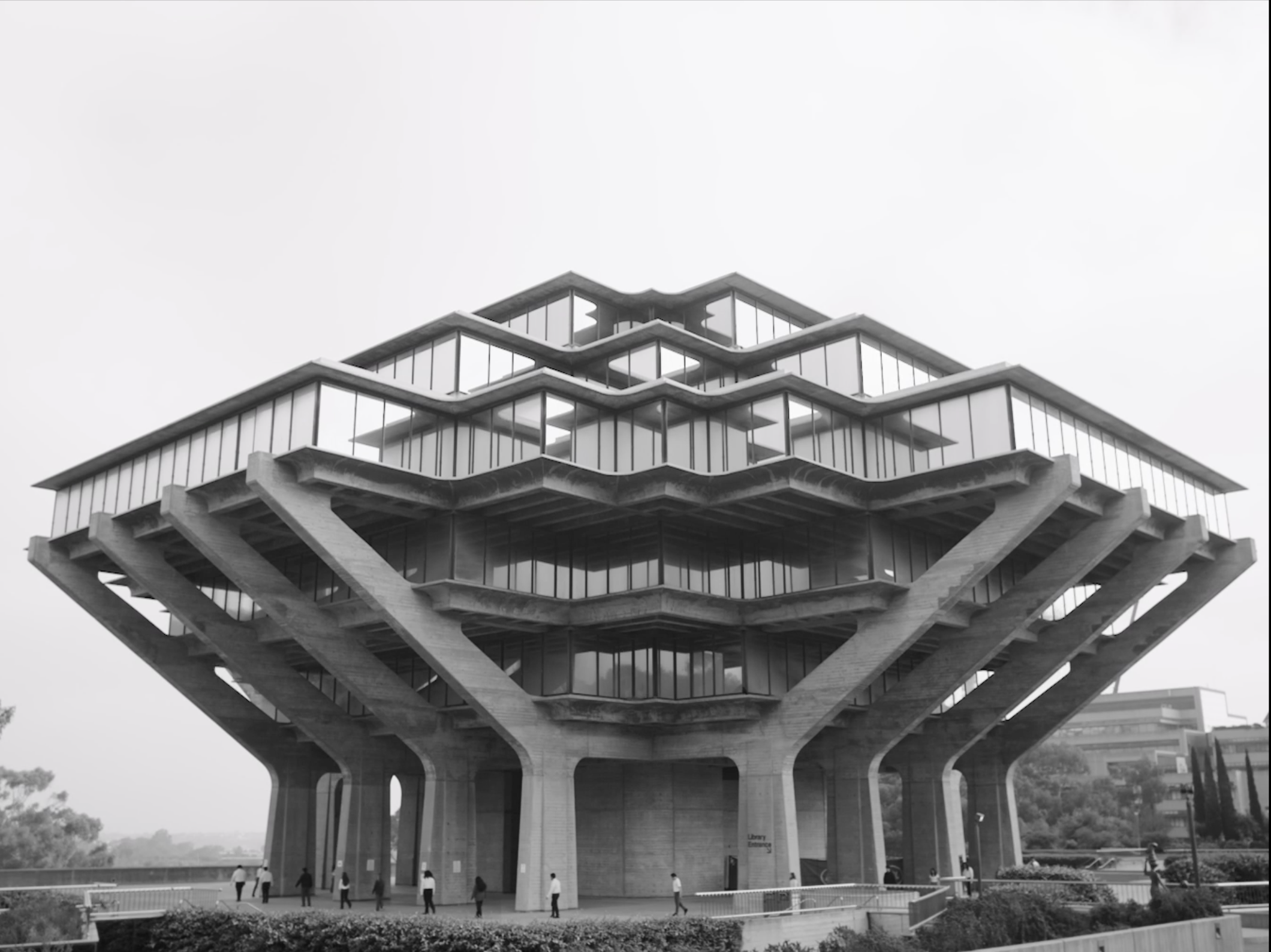 A modern multi-story building with a unique layered architectural design, supported by large concrete columns at the base, with people walking nearby in an outdoor area.