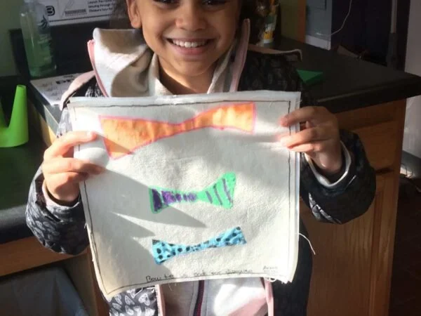 Child holding up a fabric project with colorful paper fish shapes glued on.