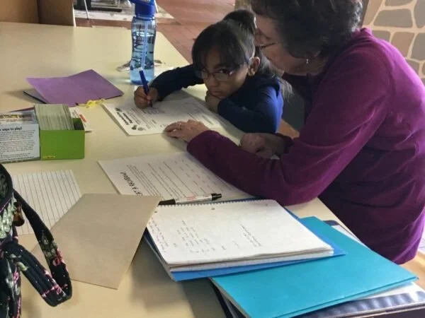 A young girl and an older woman sitting at a table with school supplies, working on homework or studying together