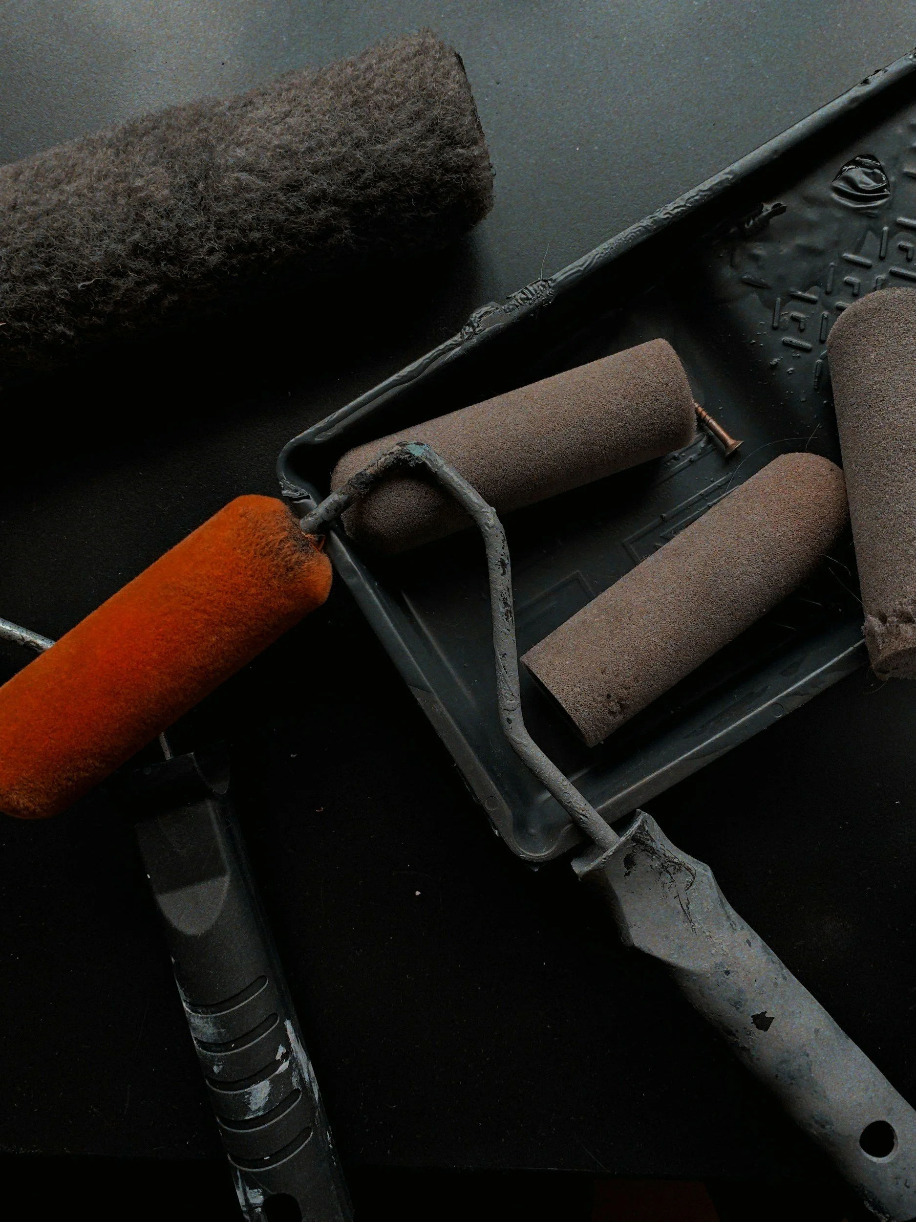 Several paint rollers with different covers on a spray painting cart, dark background.