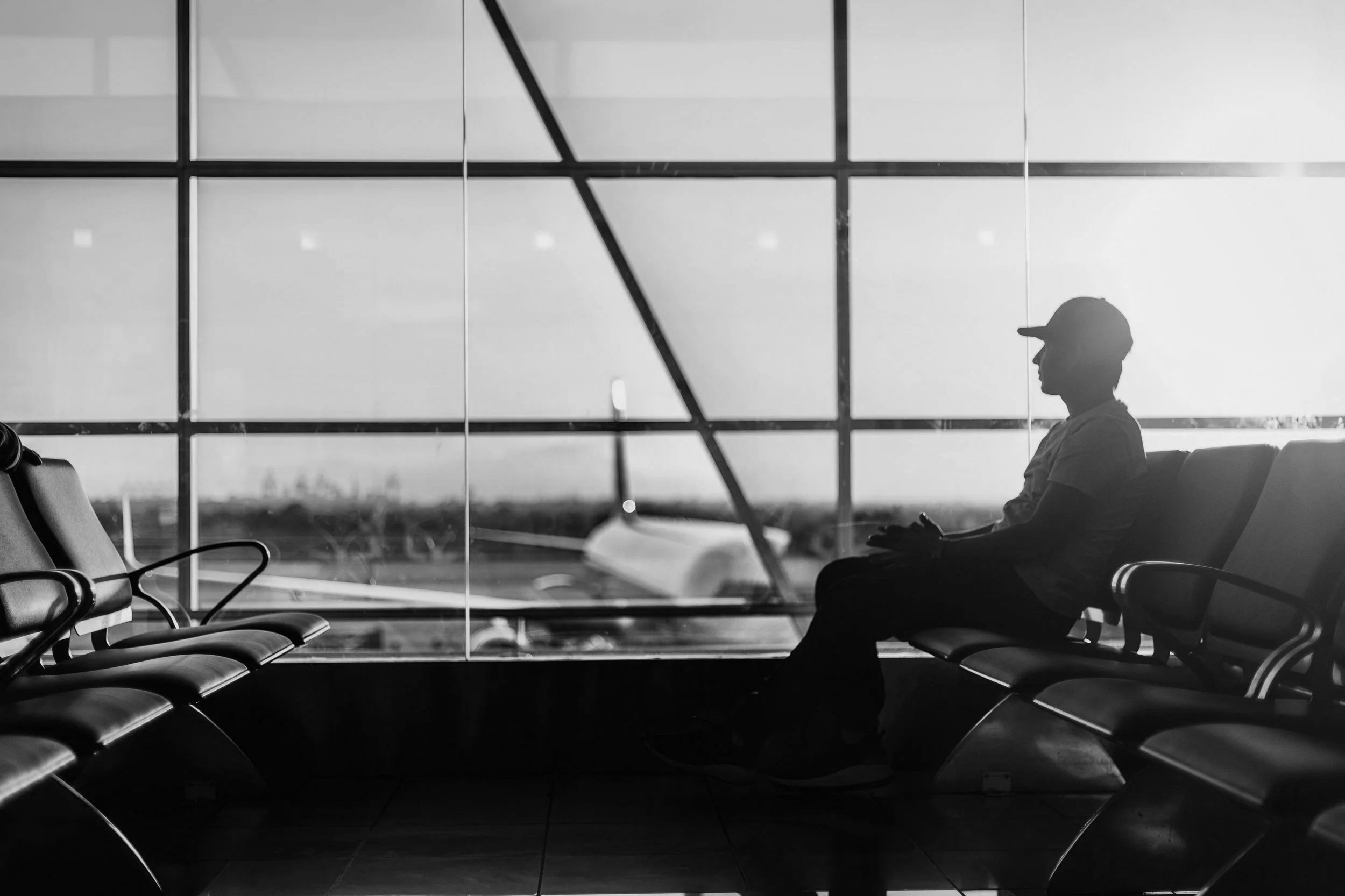 Silhouette of a person sitting while waiting at an airport terminal with large windows showing the Runway outside.