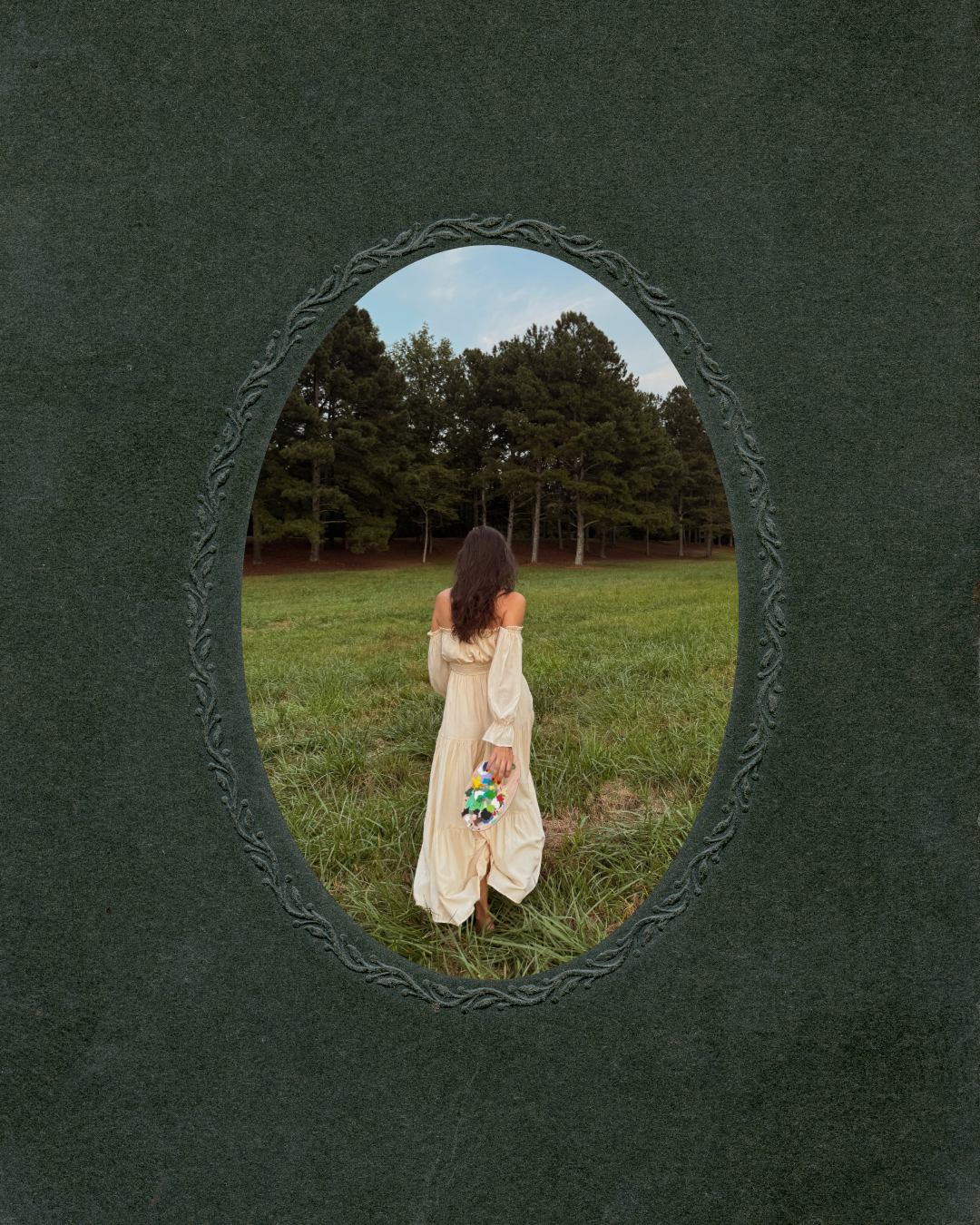 A woman in a flowing cream-colored dress standing in a grassy field, viewed through an oval-shaped mirror with decorative edges, with trees and a blue sky in the background.