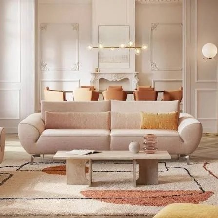 Salon moderne avec sofa beige, table basse en pierre, tapis à motifs, cheminée et murs blancs ornés de moulures.