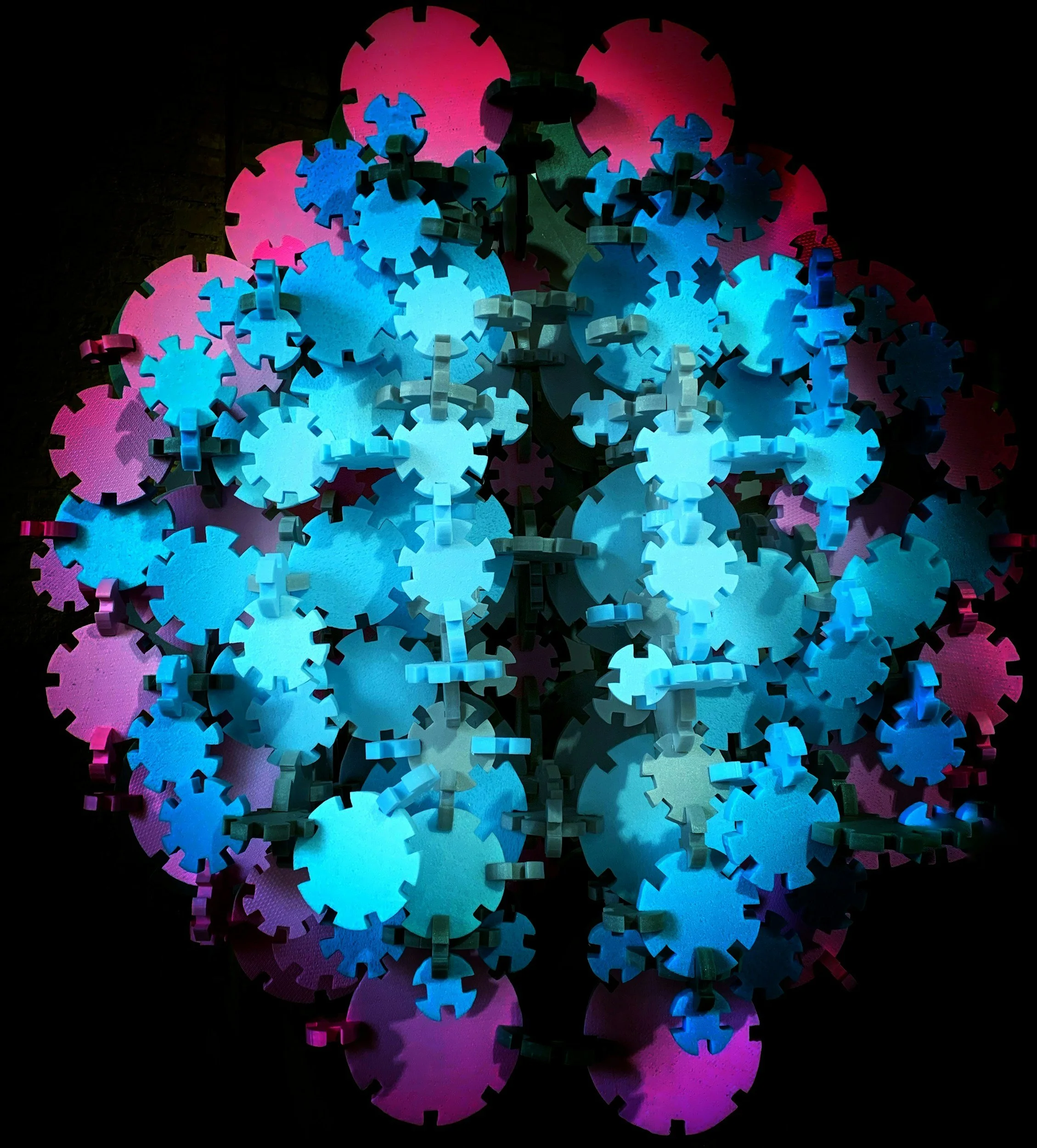 Colorful interlocking gears illuminated with pink, blue, and purple lights, reflected on a shiny black surface.