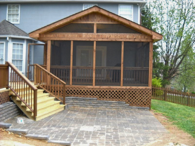 Newly built screened-in porch attached to a blue house, with wooden stairs leading up to it and a paved patio in front.