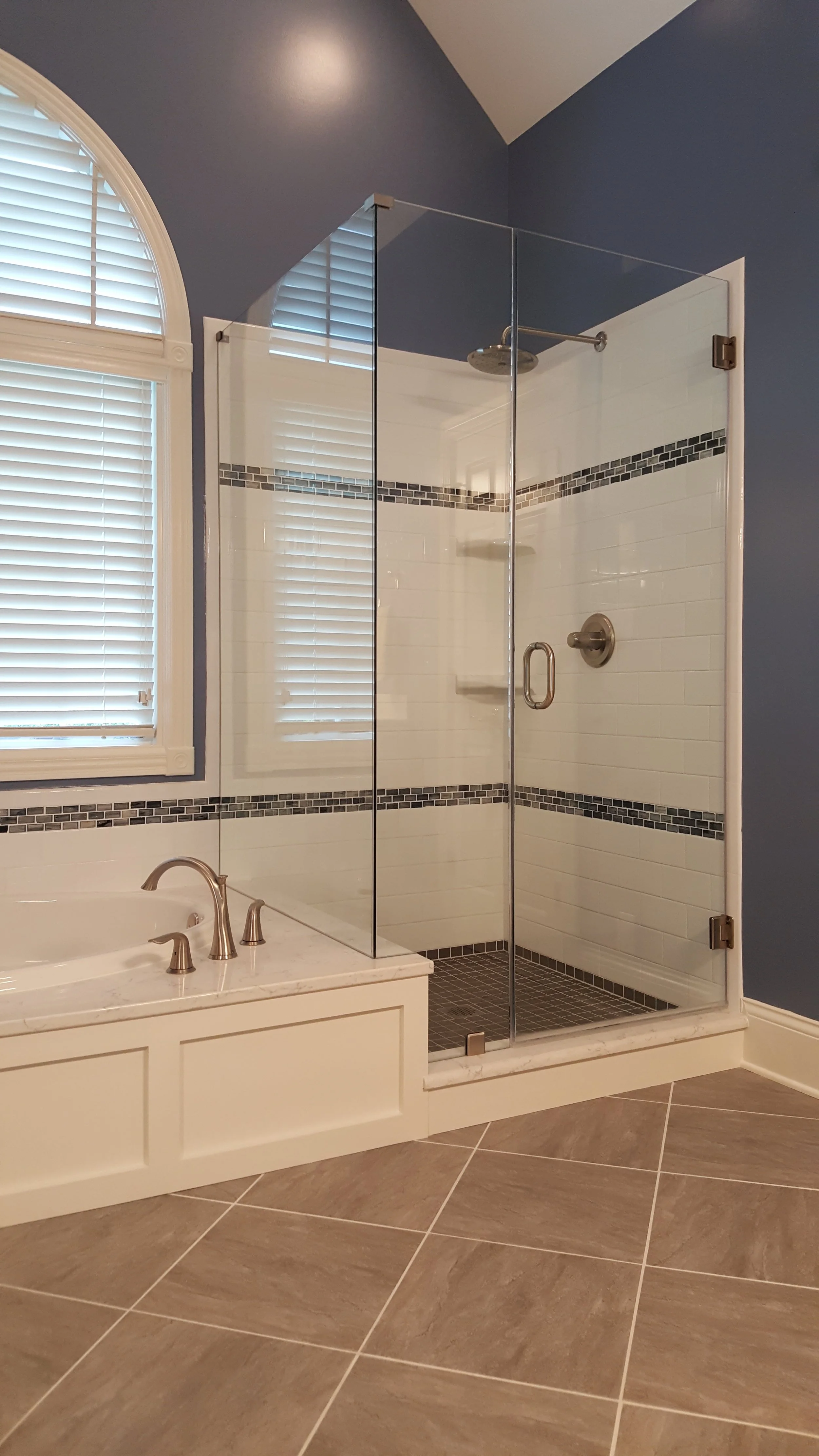 Bathroom with a glass shower enclosure, a bathtub with a faucet, large floor tiles, and a window with white blinds.