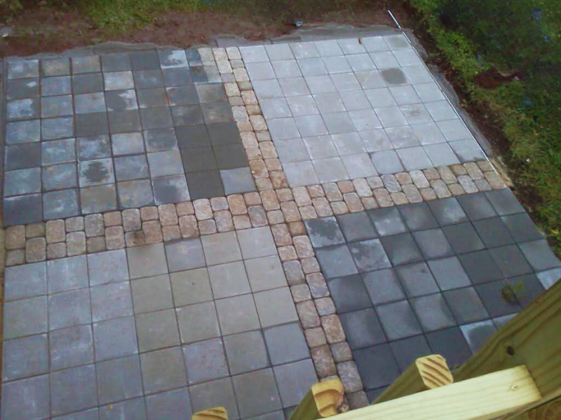 Overhead view of a tiled outdoor patio with sections of stone pavers and concrete tiles, surrounded by greenery.
