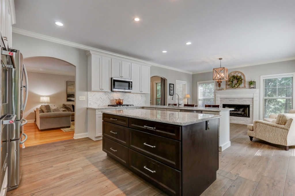 Open-concept kitchen and living room with white and dark cabinetry, granite countertops, stainless steel appliances, hardwood floors, a fireplace, and seating area.