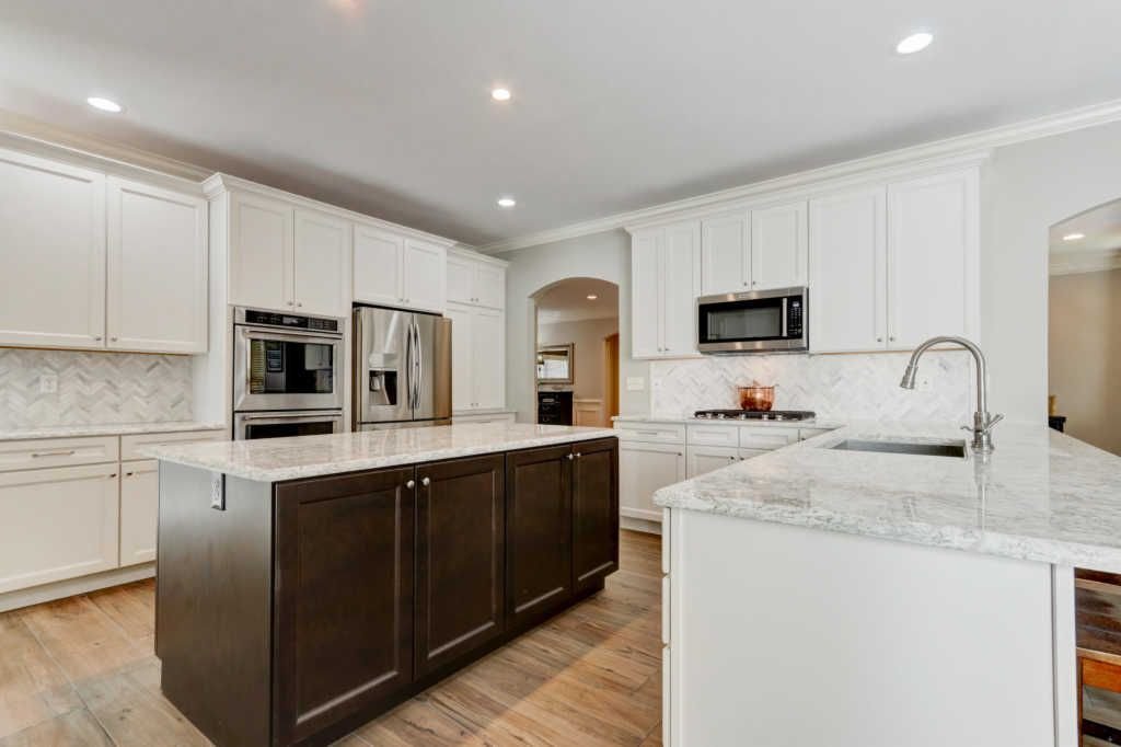 Modern kitchen with white cabinets, a dark central island, stainless steel appliances, granite countertops, and a hardwood floor.