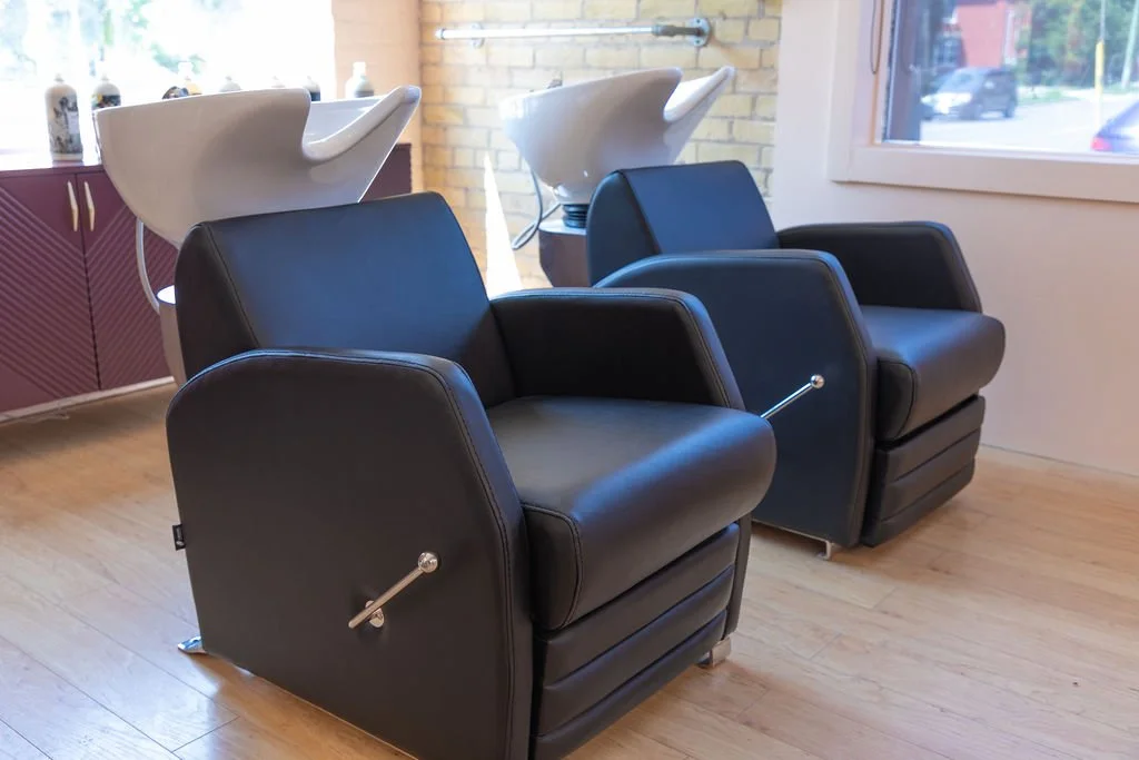 Two black salon chairs in front of white wash basins in a hair salon.