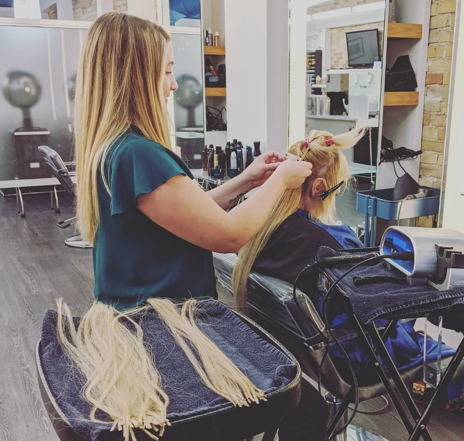 A hairstylist is curling a female client's blonde hair in a salon.