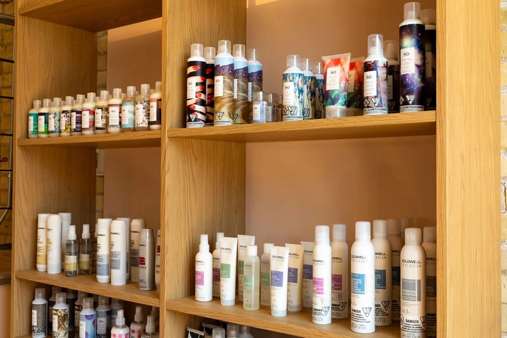 Shelf filled with bottles of hair and skincare products. Wooden shelving unit with multiple rows of variously colored bottles and containers.