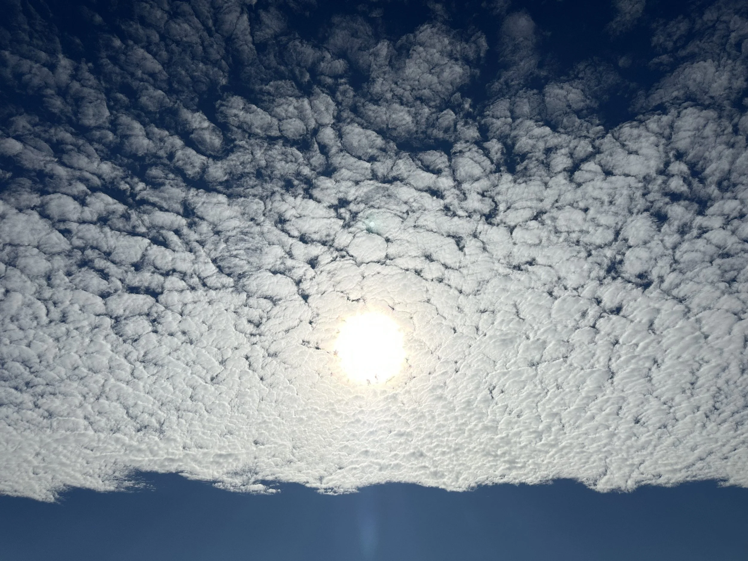 A view of a cloudy sky with the sun partly visible at the bottom, illuminating the clouds.