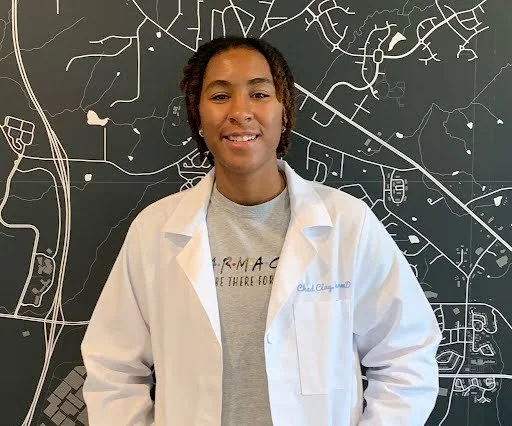 A woman in a white lab coat standing in front of a large blackboard or map with white lines and shapes.