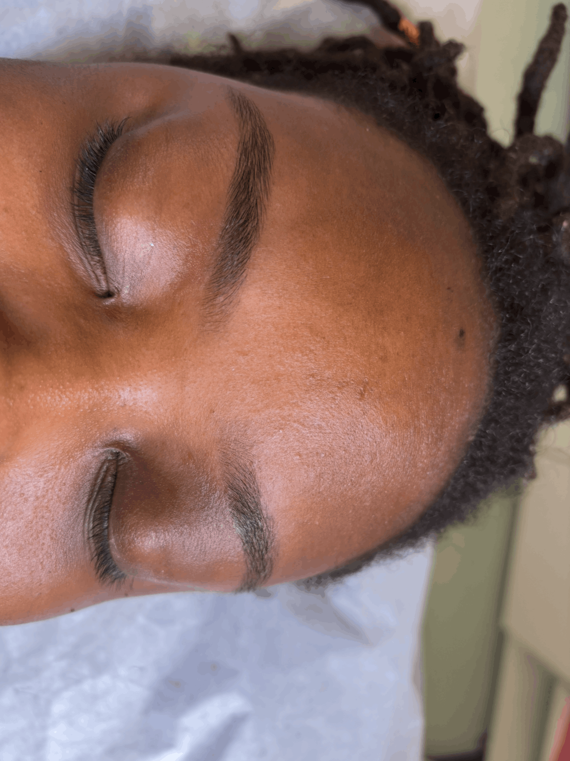 Close-up of a person's face with closed eyes, showcasing natural makeup and textured skin.