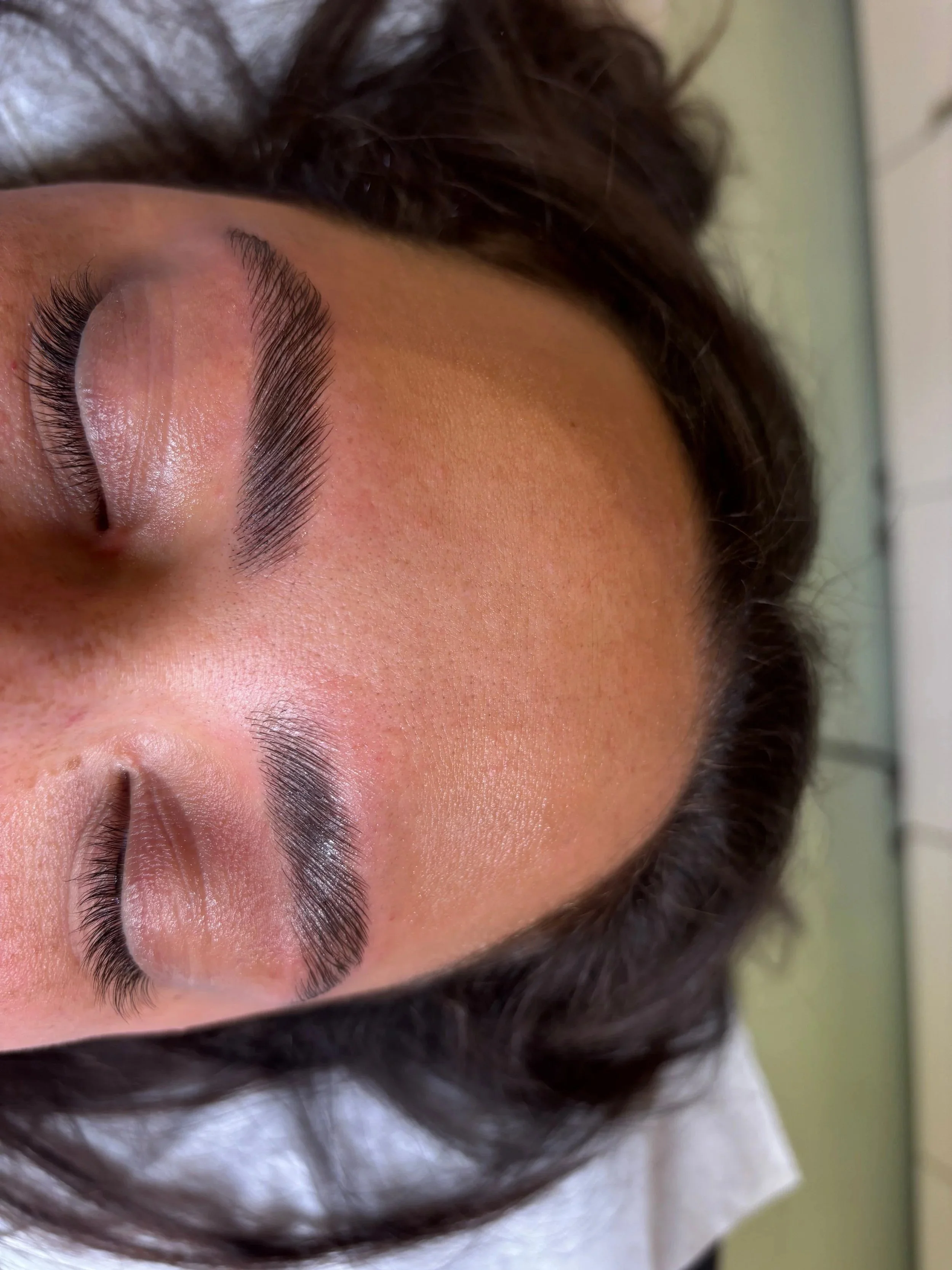 Close-up of a person's face showing their eyebrow, eye, and part of their cheek, with dark brown hair partially covering their head.