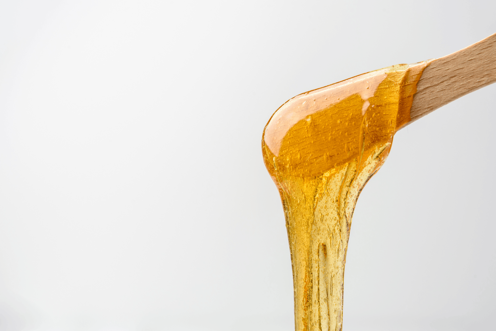 Close-up image of honey being poured from a wooden honey dipper.