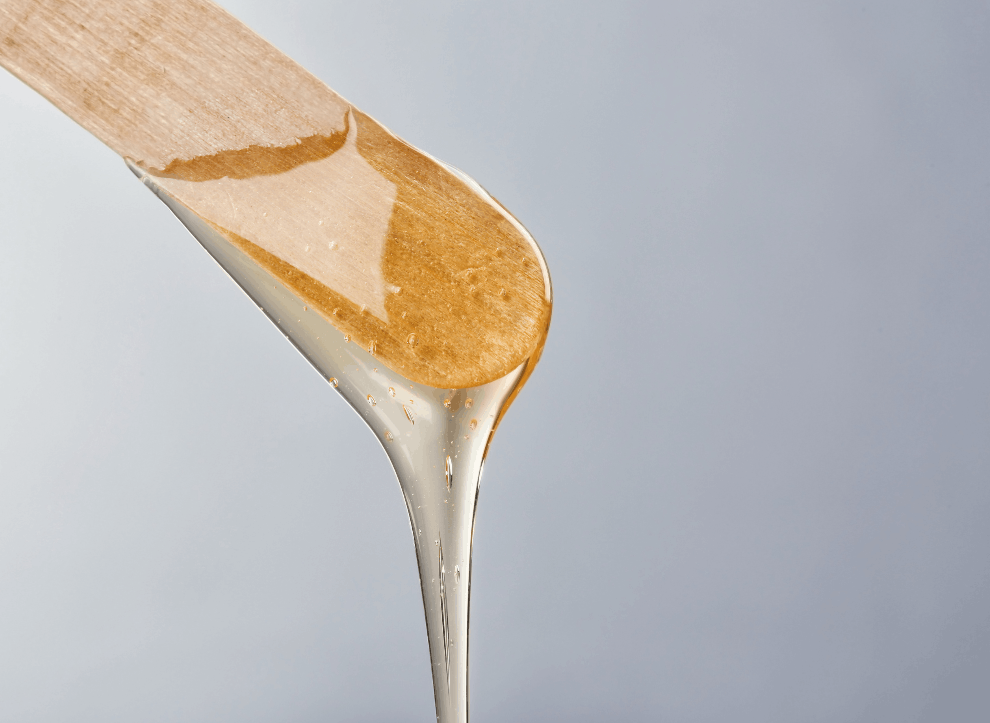A wooden spatula drizzling honey onto a surface, with honey falling from the spatula.