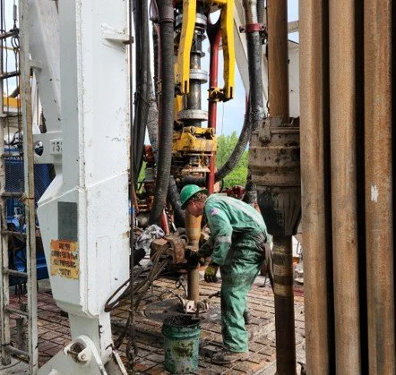 Worker in green overalls using a geothermal drill