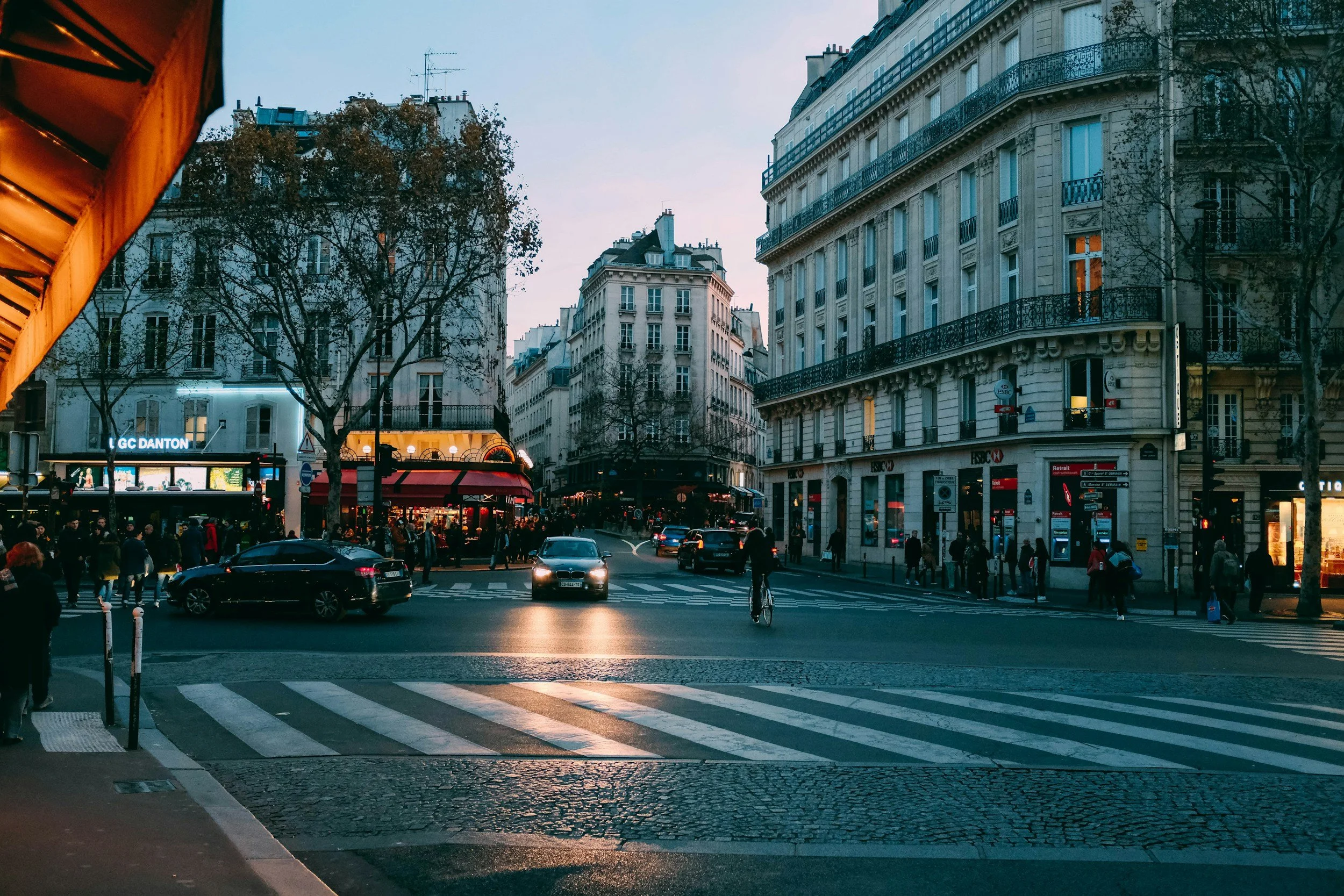 Scene of a lively street corner filled with people in Paris at dusk.
