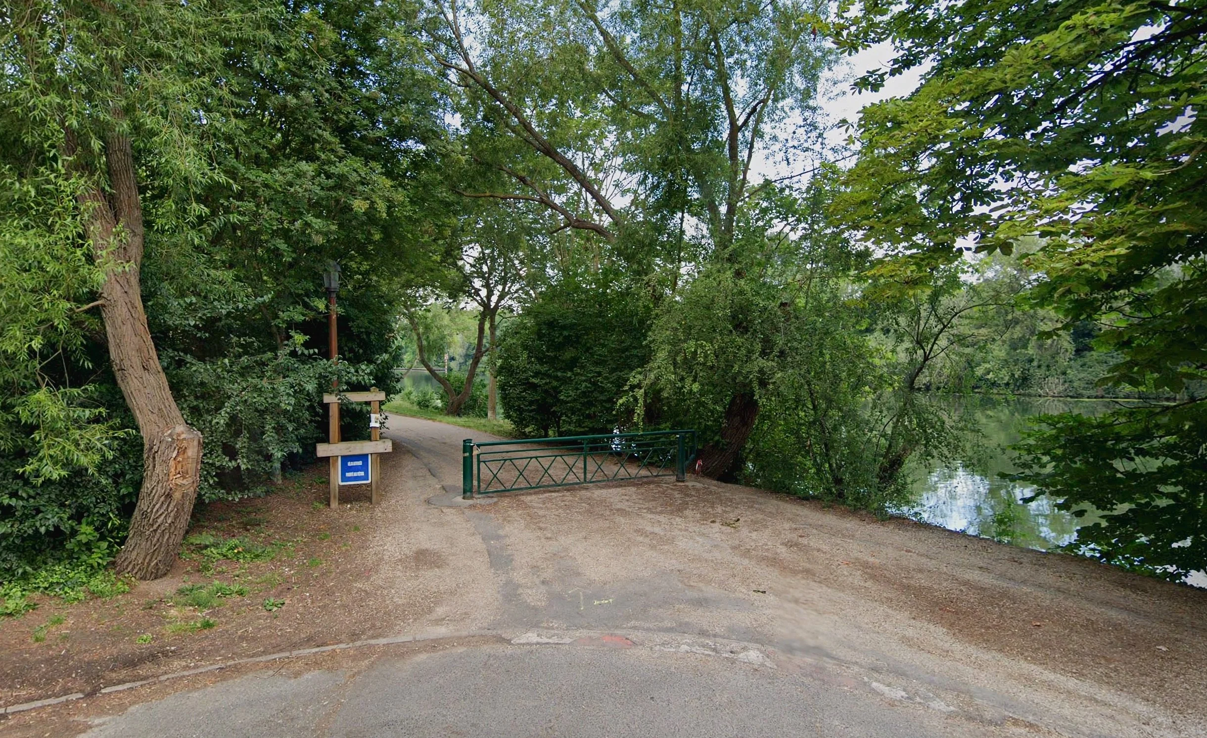 A quiet gravel path bordered by willow trees, ending at a low green gate along the riverbank