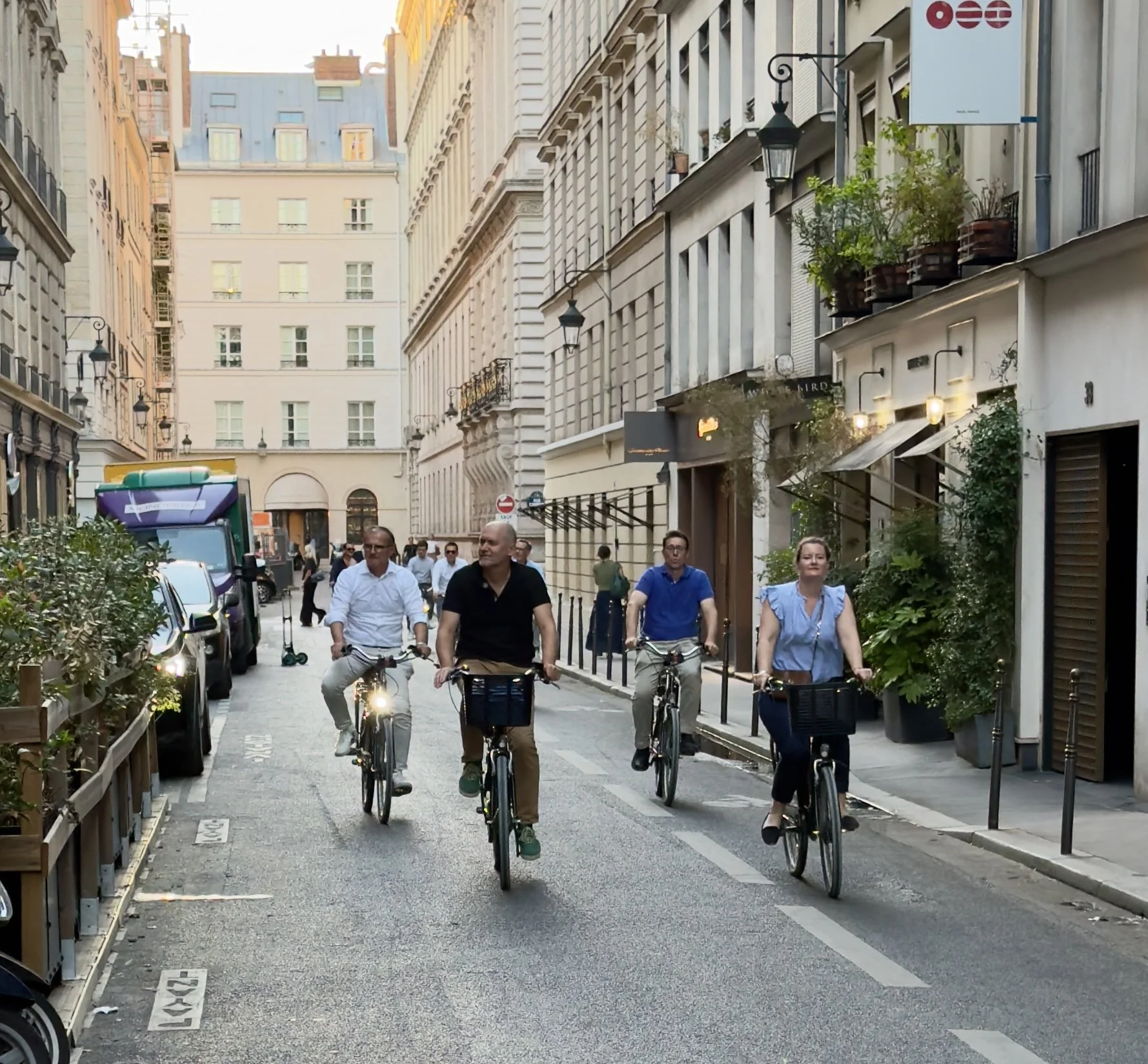 Four cyclists riding together down a narrow Paris street lined with shops and evening lights