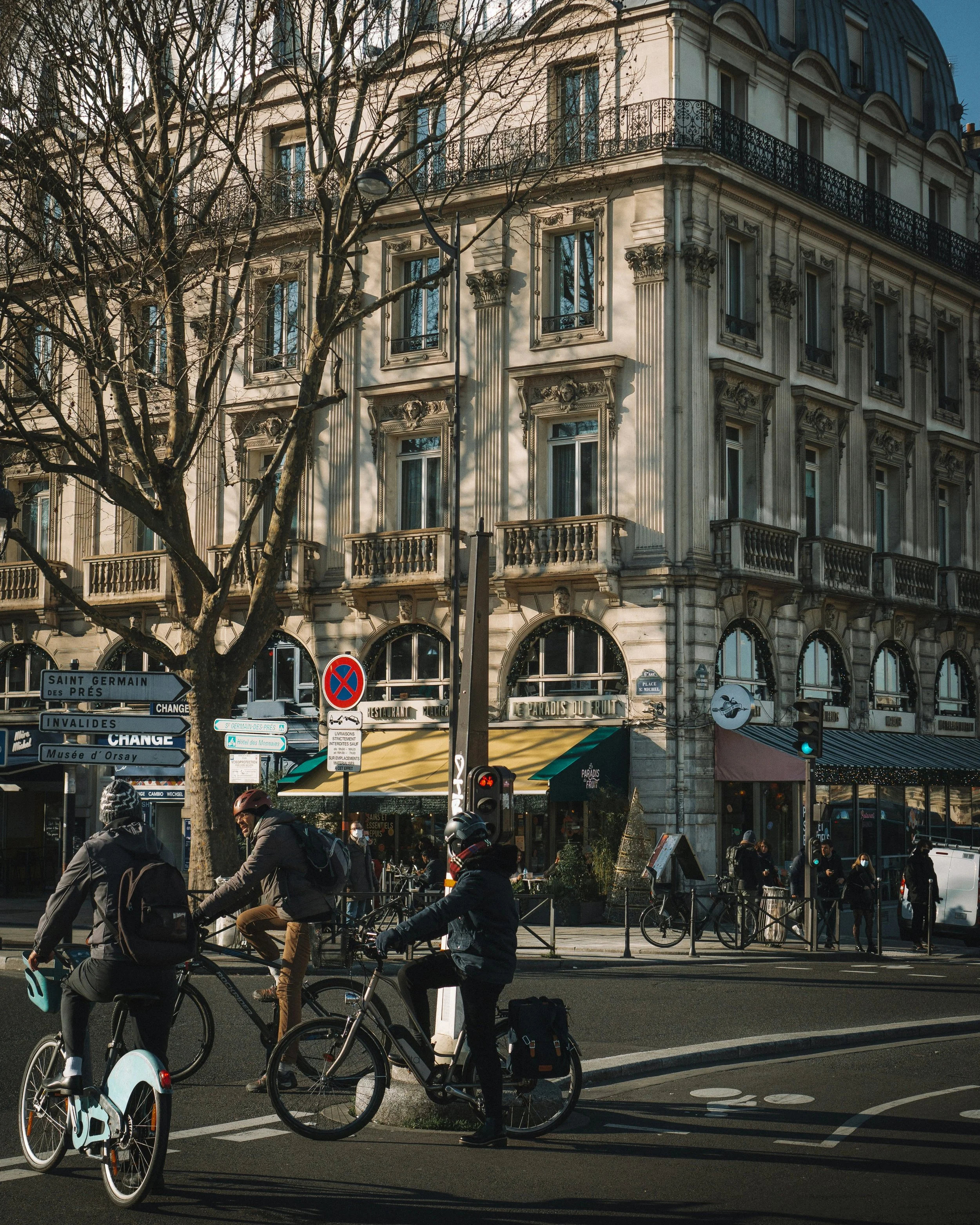 Three cyclists stopped at a traffic light on a Left Bank Paris street near signs for Saint-Germain-des-Prés and Musée d'Orsay