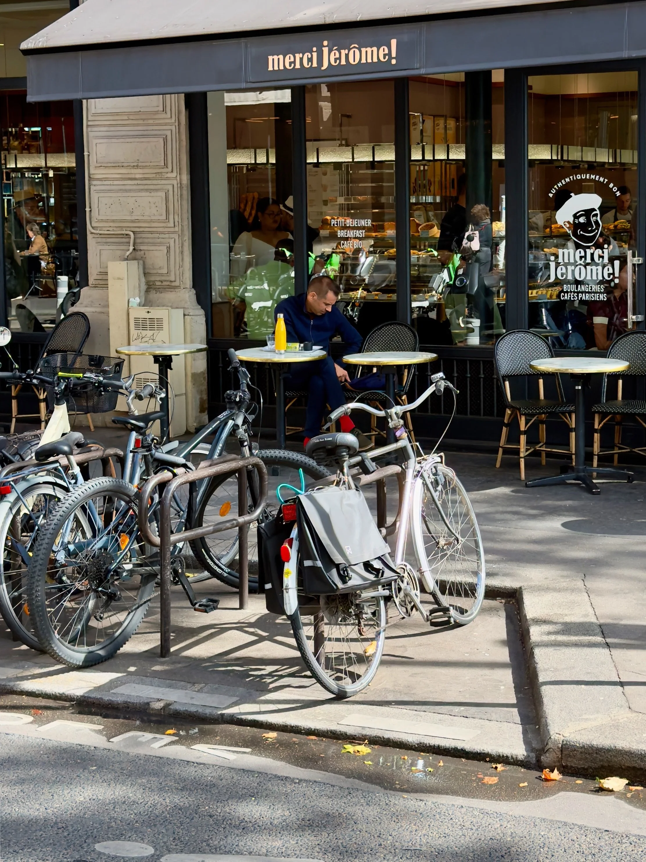 Row of bicycles parked outside a Paris café and bakery, with a cyclist seated at an outdoor table