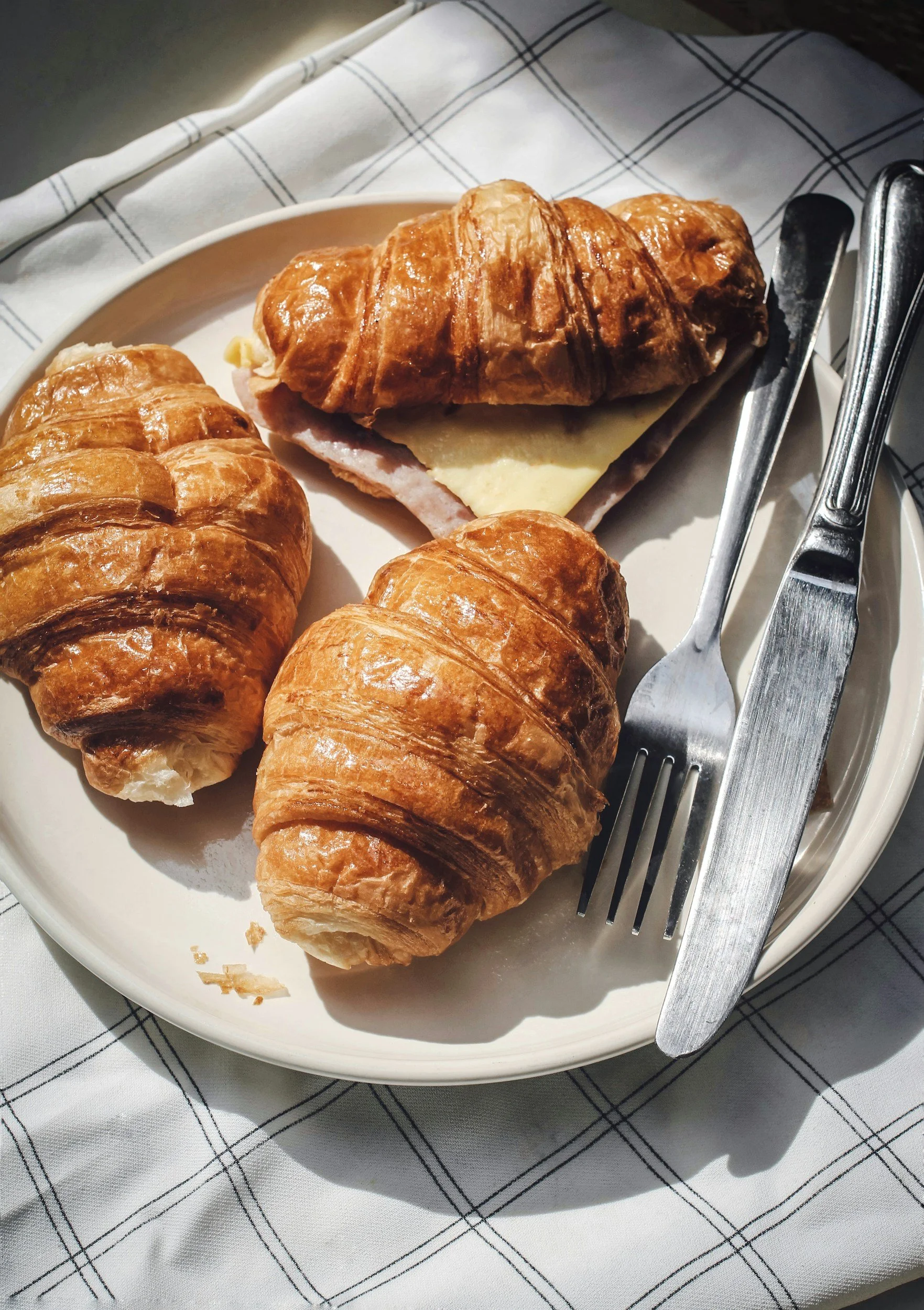 Three various pastries on an off-white plate, with cutlery.