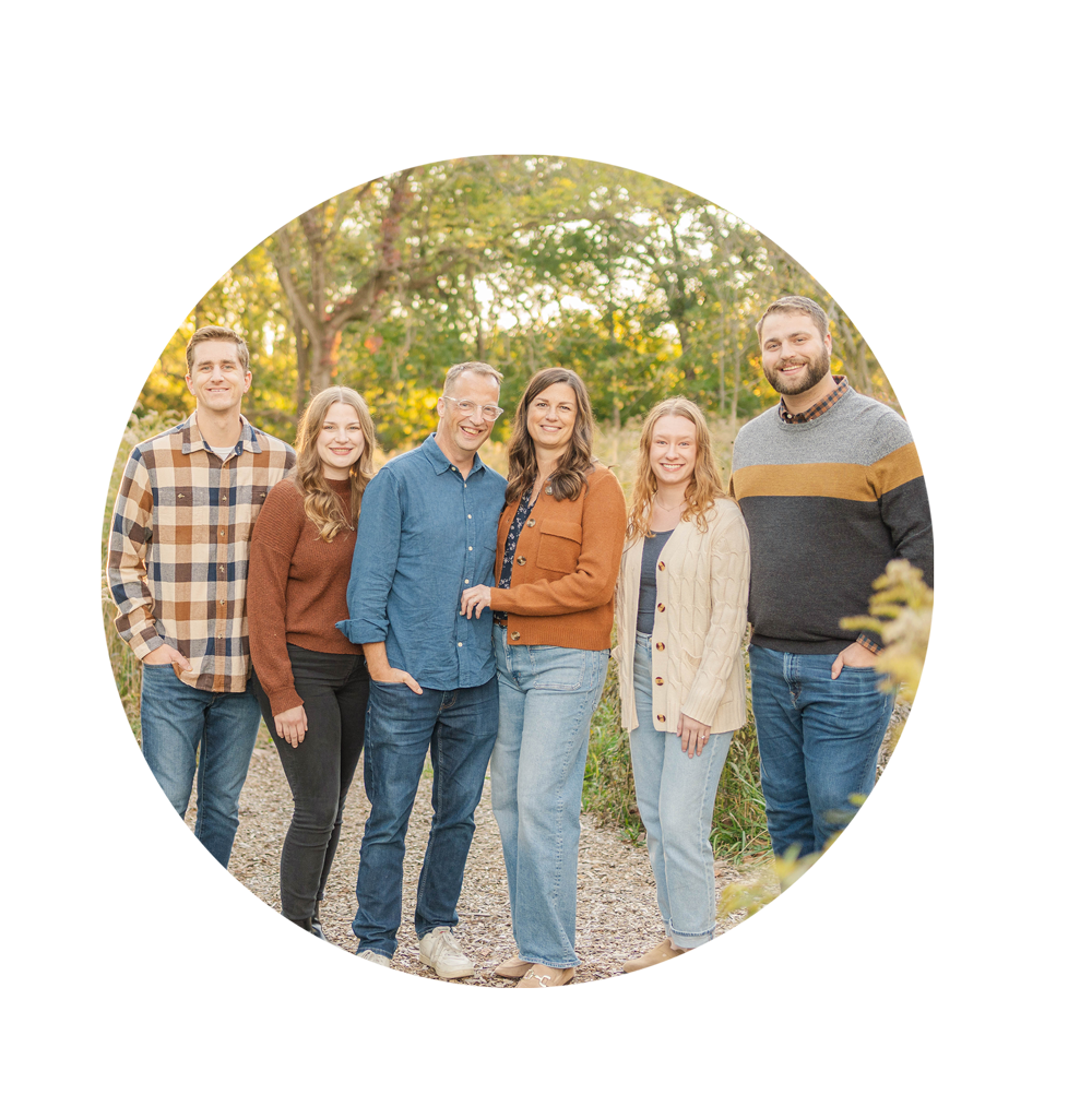 Six people standing outdoors on a trail surrounded by trees with autumn foliage, smiling at the camera.