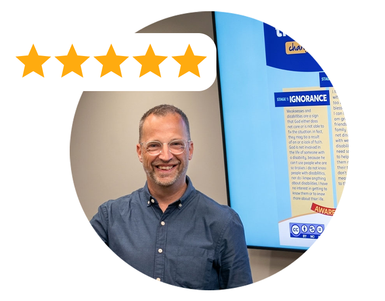 A smiling man wearing glasses and a blue shirt standing in front of a presentation screen with text about ignorance and awareness.