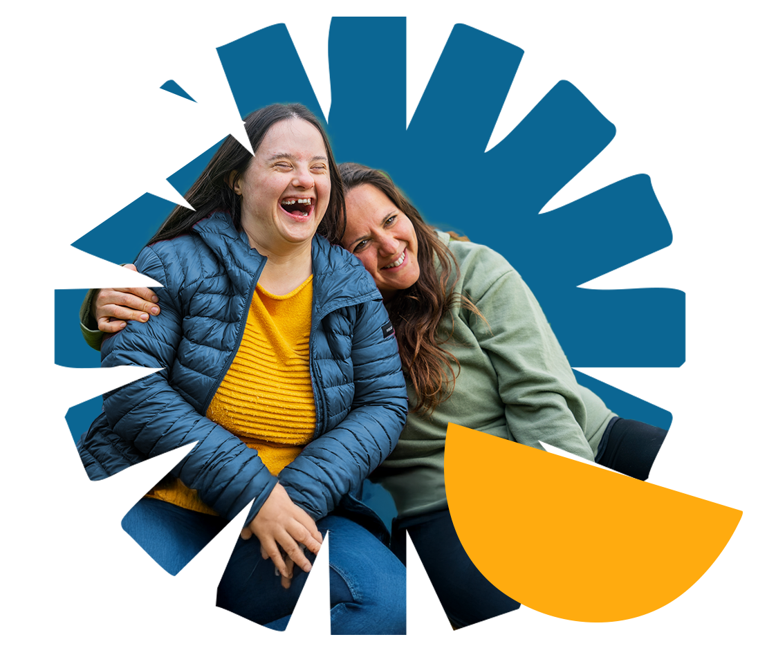 Two women sitting close together, smiling and laughing, with one woman embracing the other, against a background with blue and orange abstract graphics.