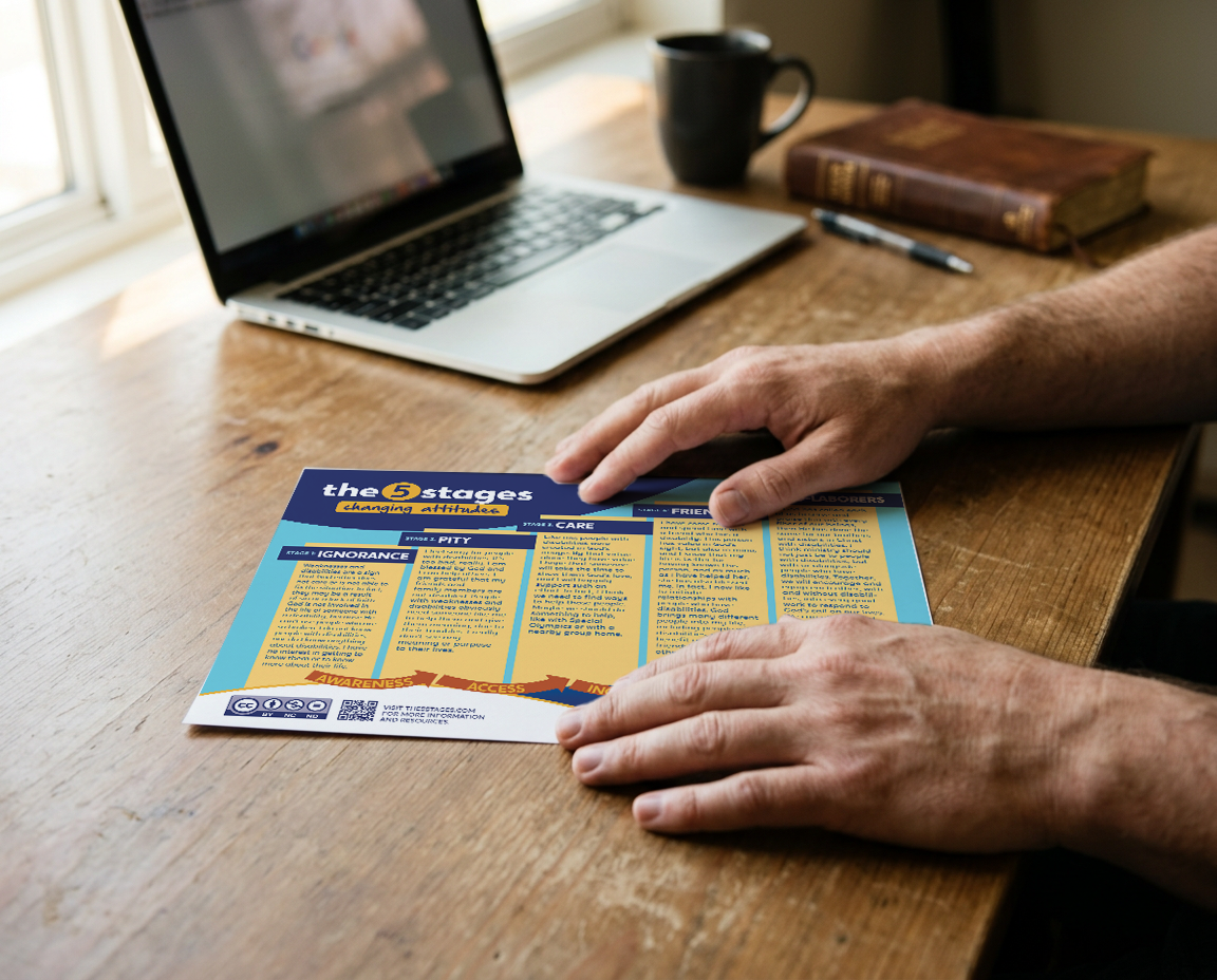 Person holding a colorful informational pamphlet titled 'the 5 stages changing attitude' on a wooden desk.