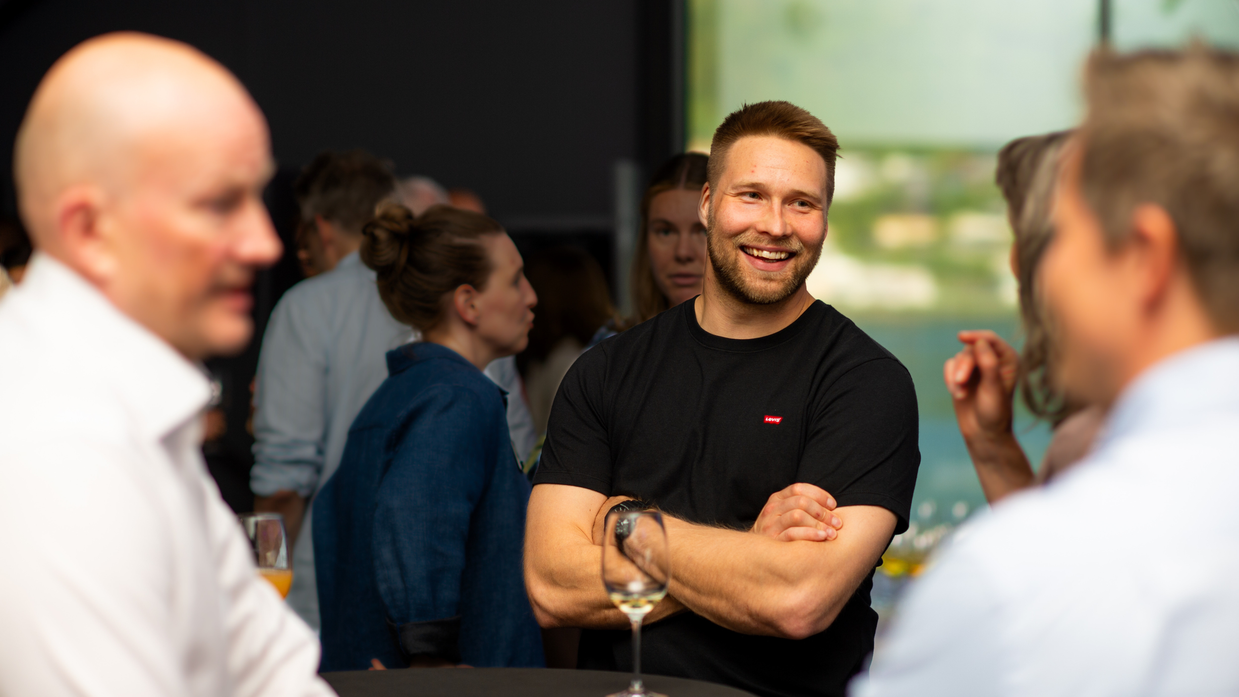 People socializing at an indoor event, with Krister Halonen smiling and engaging in conversation, surrounded by others in professional setting.