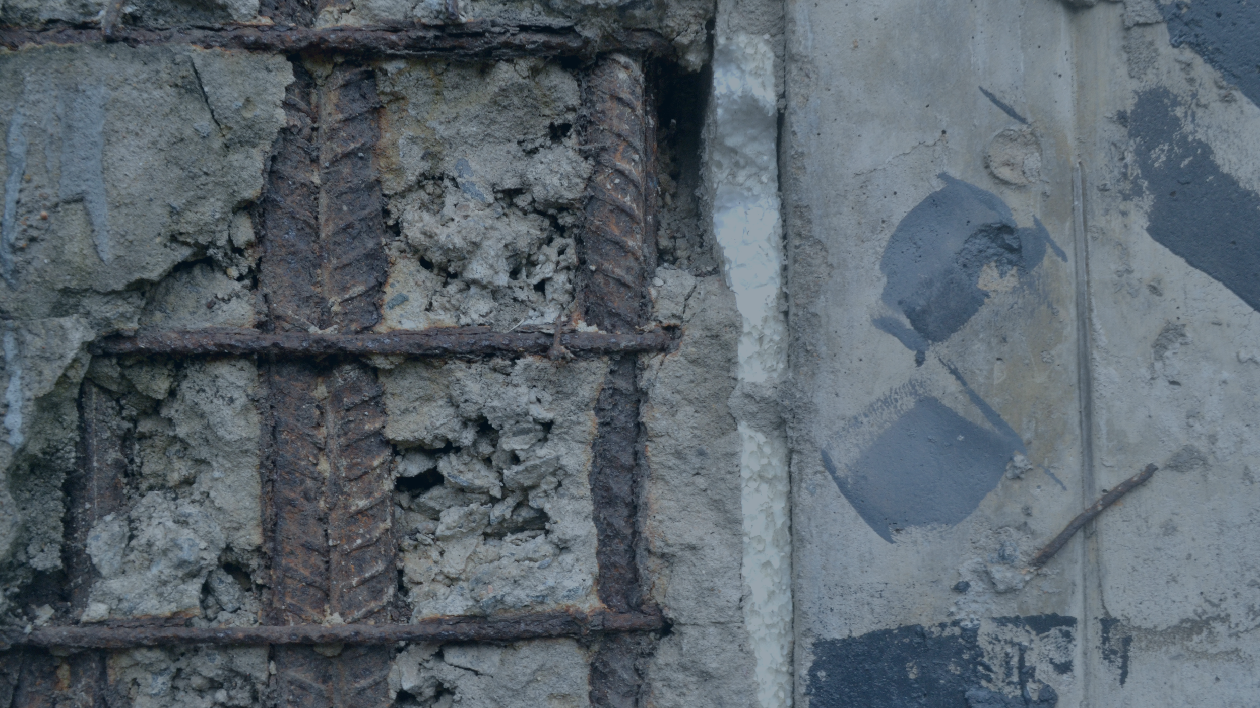 Close-up of a section of a concrete wall with exposed rusted steel rebar and crumbling concrete.