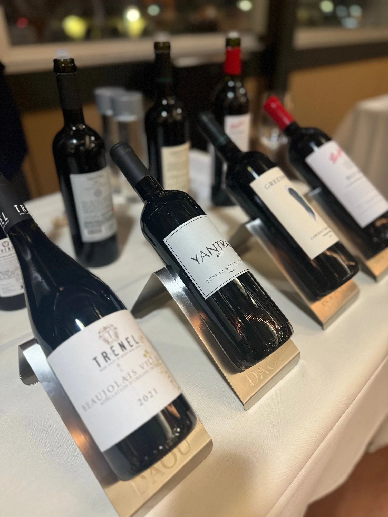 Several bottles of wine displayed on a table, supported by gold-colored stands, with labels indicating the names and vintages at the Thief Wine Grand Tasting in Milwaukee.