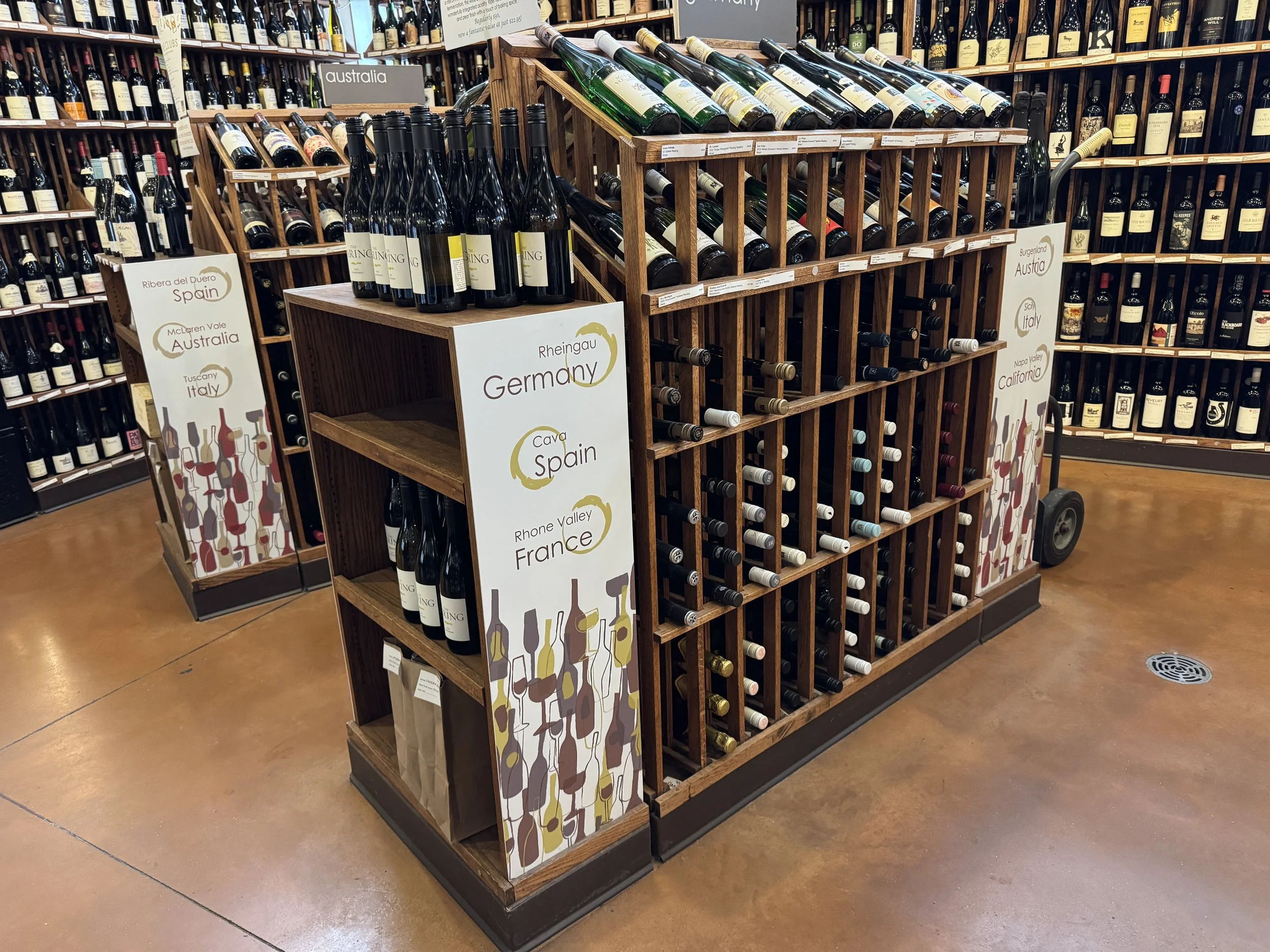 A display of wine bottles at Thief Wine Shop and Bar in Milwaukee with a wooden wine rack and signs indicating different regions such as Germany, Spain, Italy, and France.