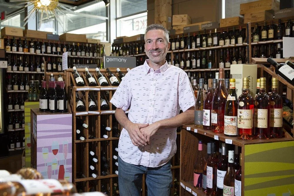 Phil Bilodeau, owner of Thief Wine Shop and Bar, surrounded by shelves filled with bottles of wine from various countries.