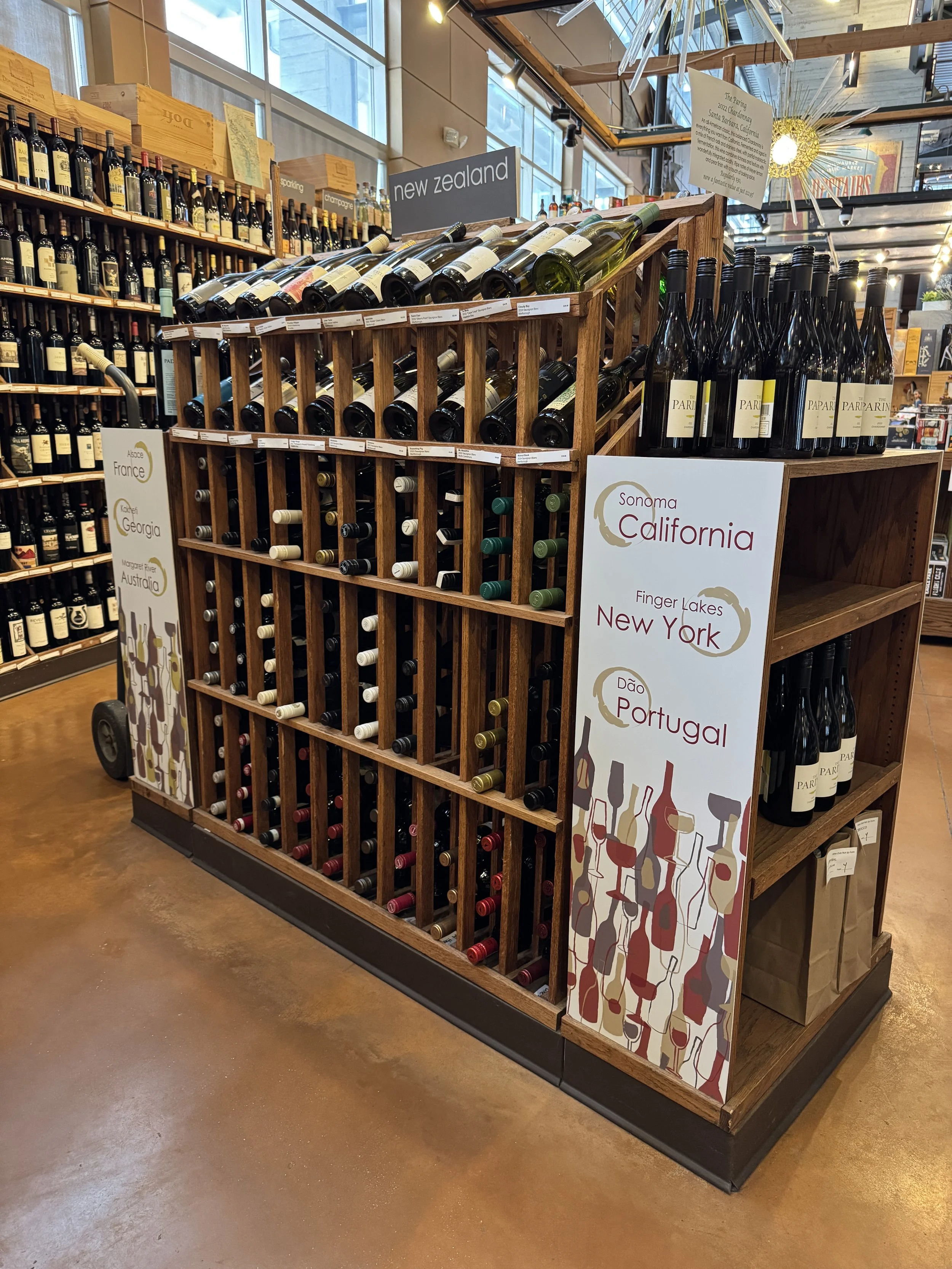 A wine display at Thief Wine Shop and Bar in the Milwaukee Public Market with bottles in the background and signs indicating wines from New Zealand, California, Sonoma, Finger Lakes, and Portugal.