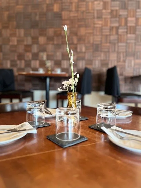 Table set with four plates, four upside-down glasses, and a centerpiece with white flowers in a gold vase at a restaurant.