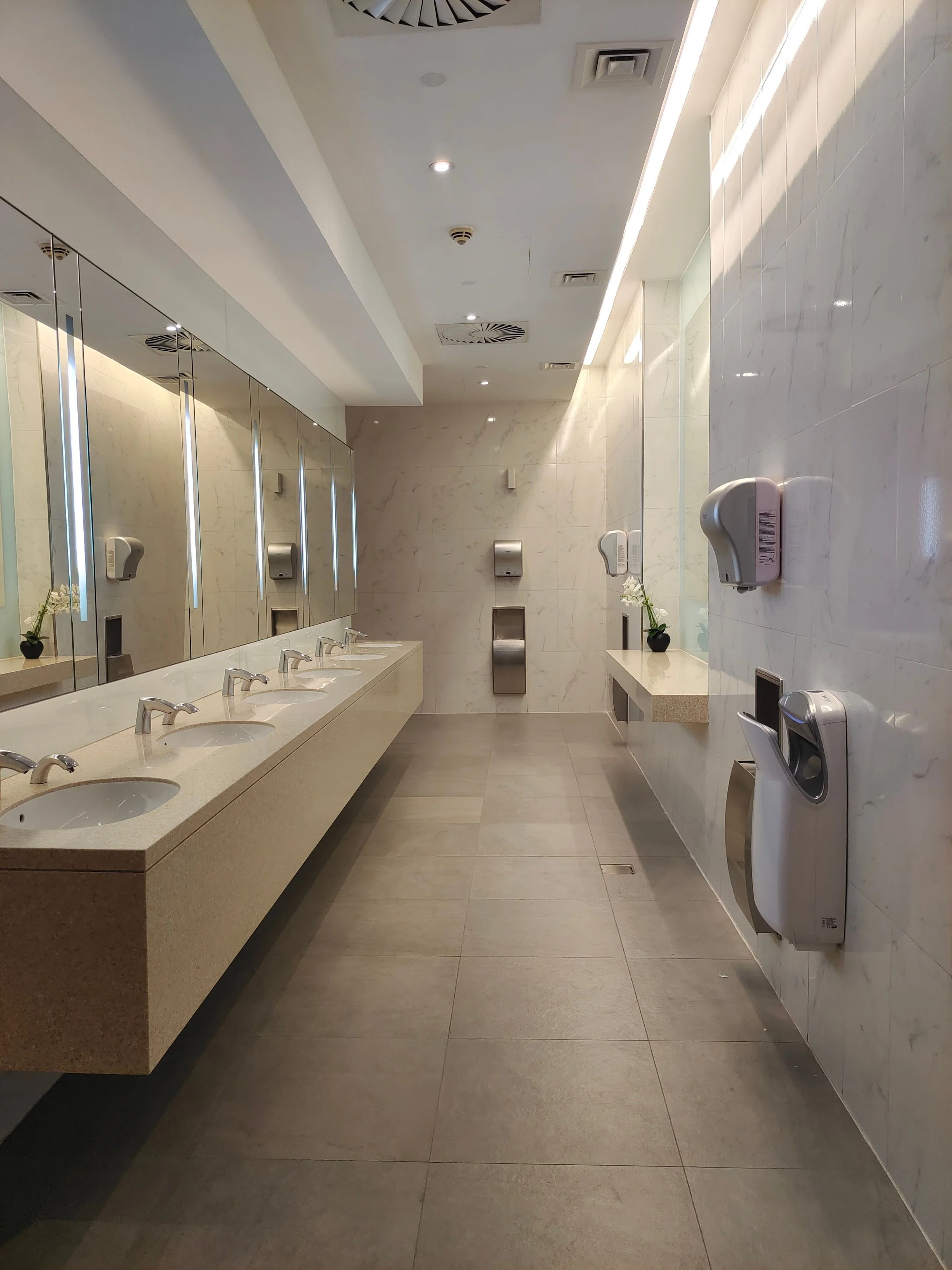 Public restroom with multiple sinks, soap dispensers, and mirrors on the wall.
