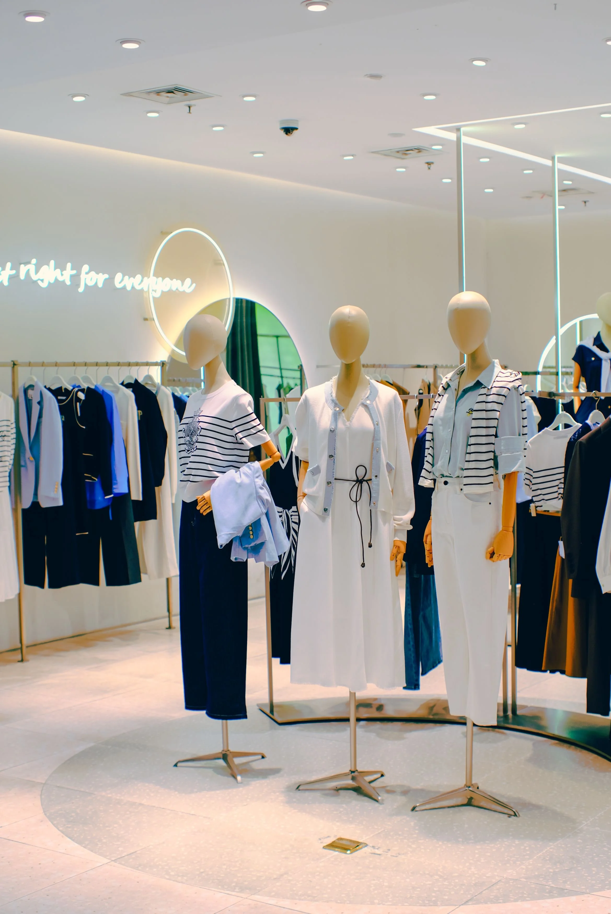 mannequins dressed in casual and formal clothing inside a clothing store with racks of clothes in the background.