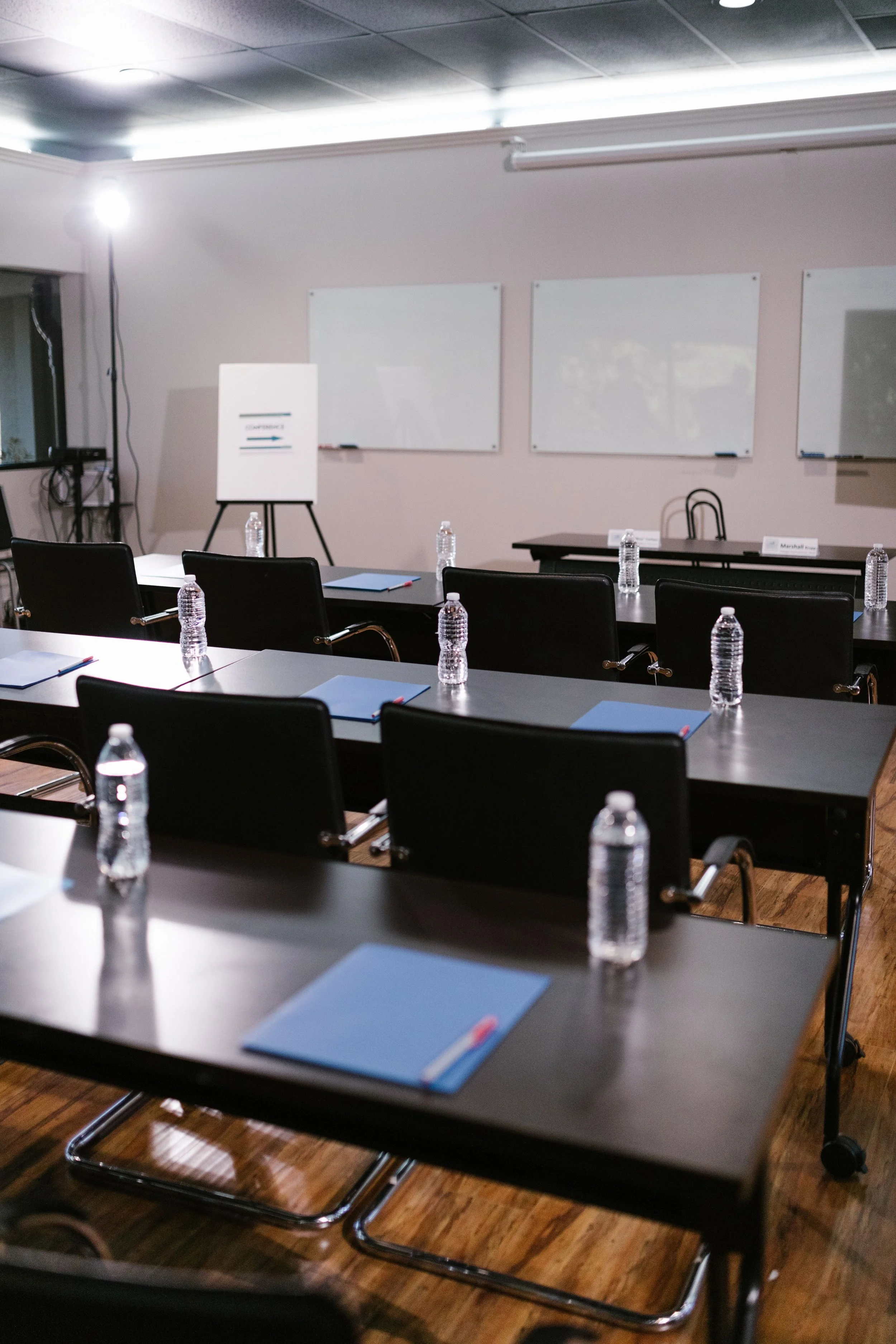 A conference room with black tables and chairs, a whiteboard, and several water bottles on the tables.